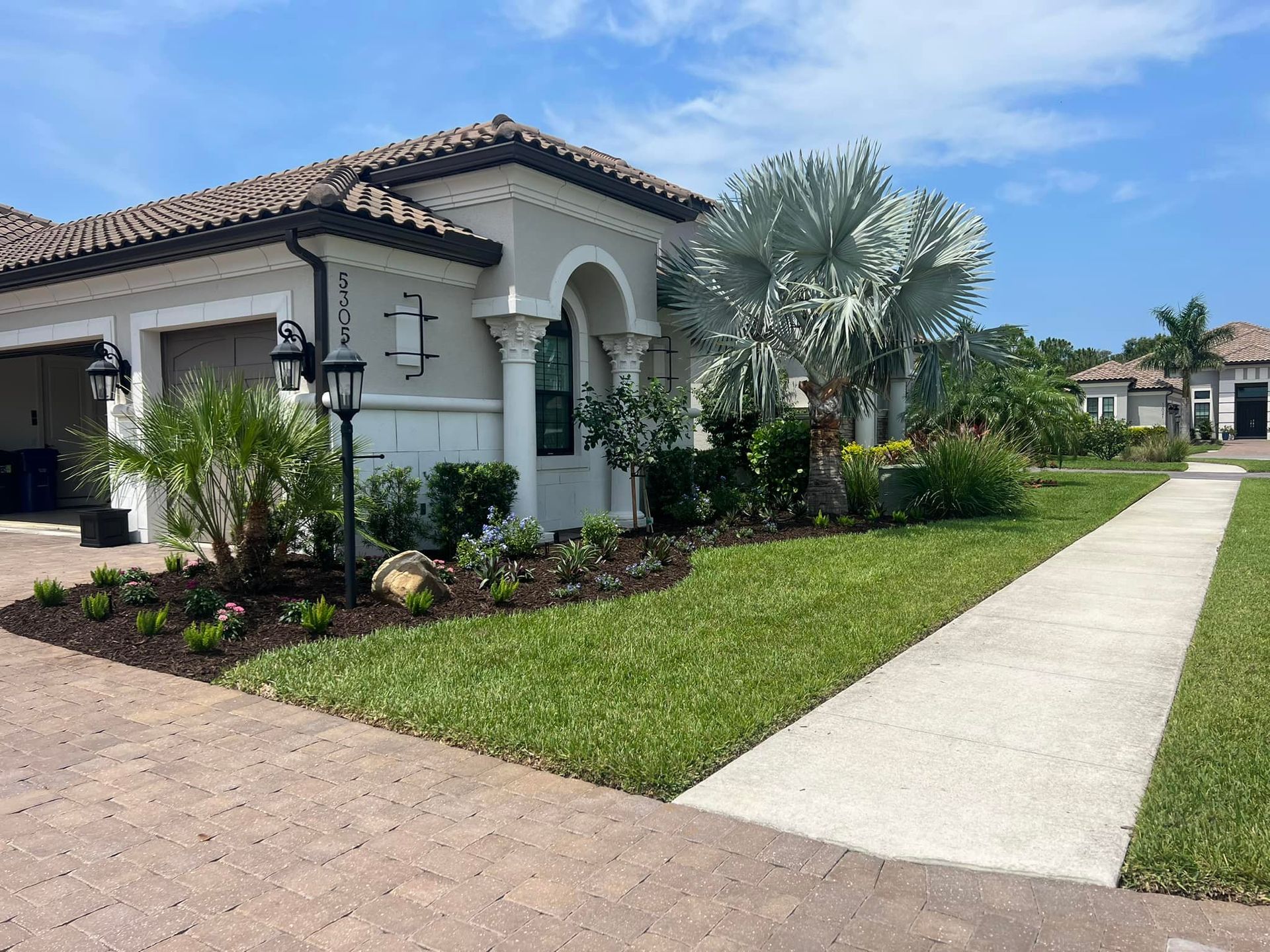 House with beige exterior, green lawn, sidewalk, and landscaping under a sunny sky.