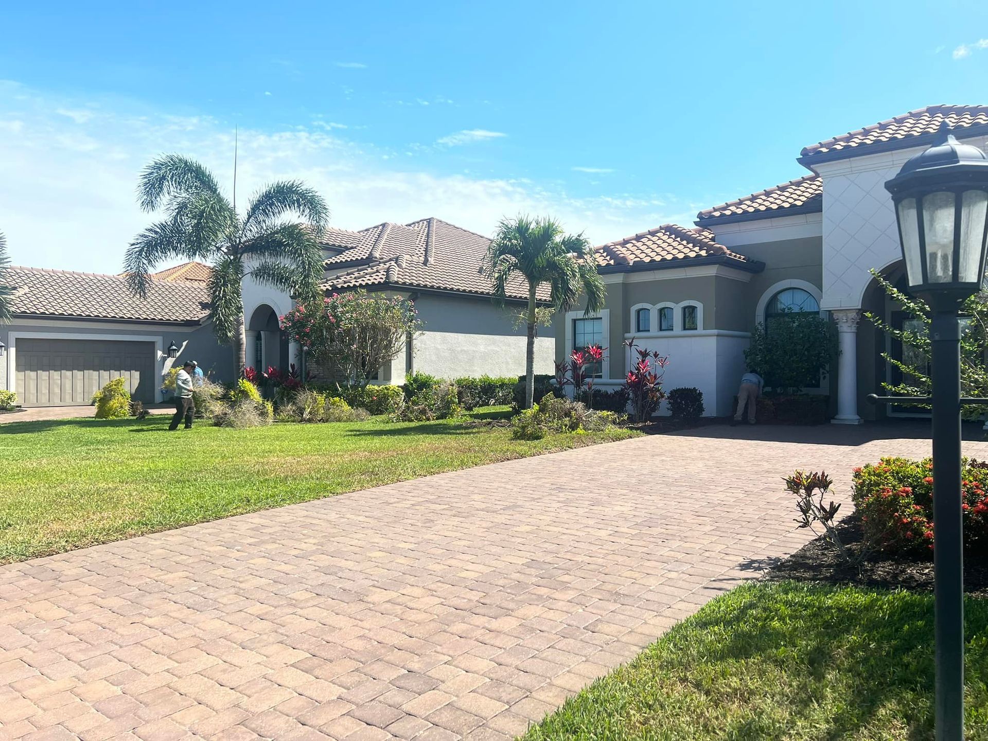 A house with a brick driveway, lawn, and a light post on a sunny day.