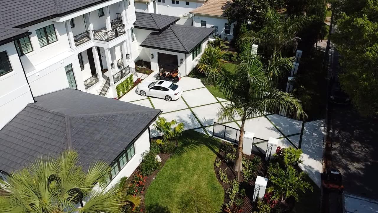 Aerial view of modern white houses with black roofs and a car parked in the driveway. Lush landscaping.