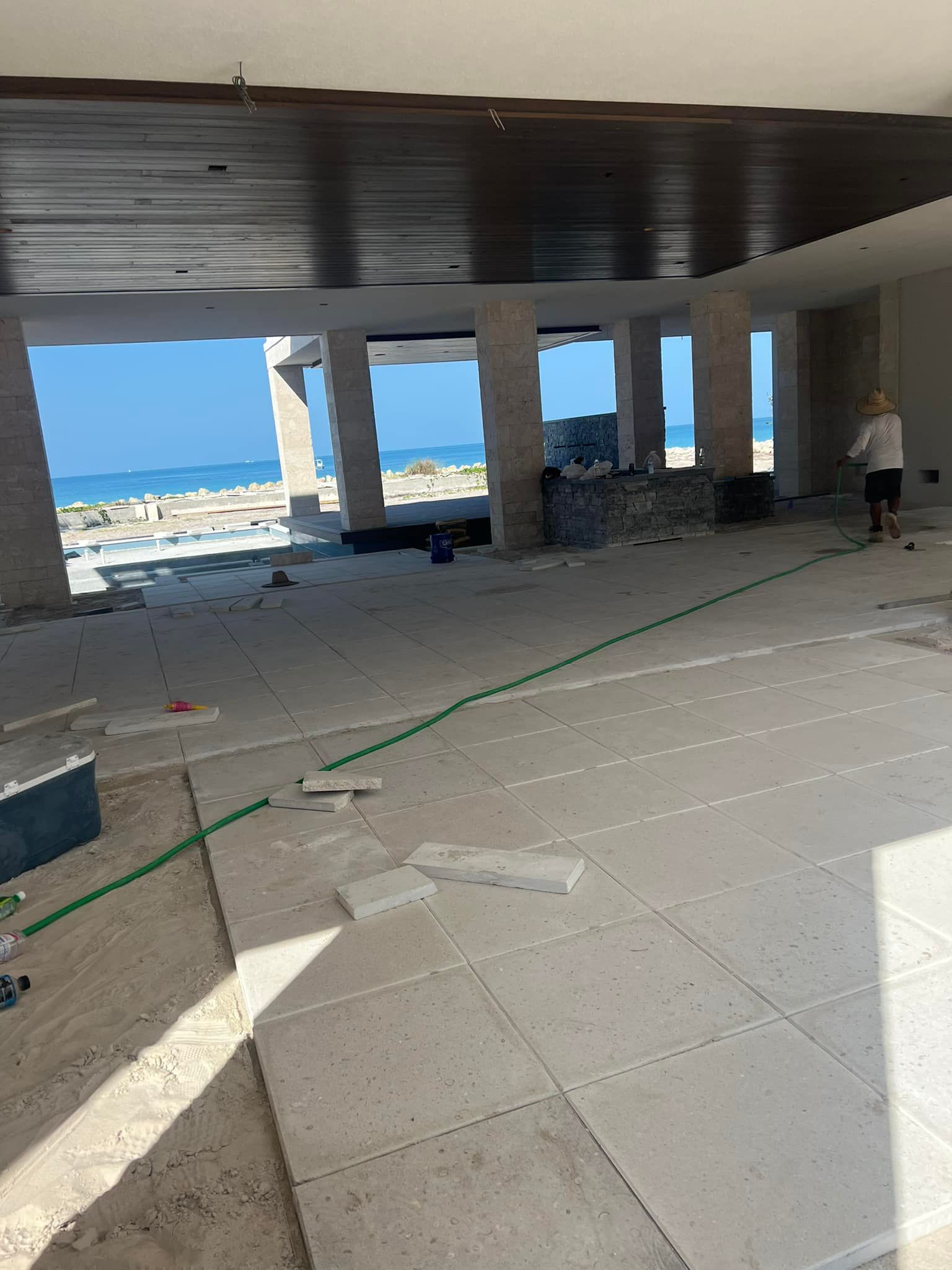 Construction site with ocean view; unfinished interior, tile flooring, columns, and a person.