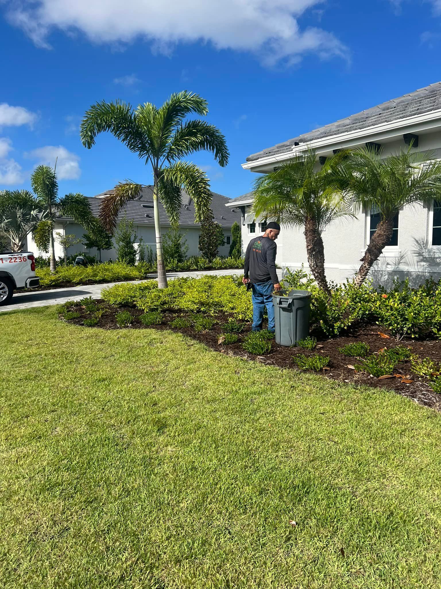 Man tending garden in front of a white house on a sunny day.