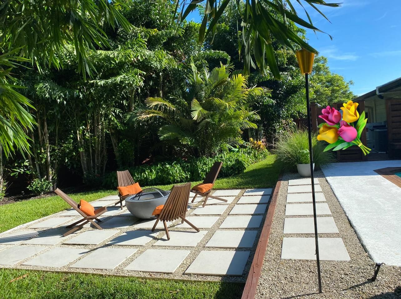 Patio with fire pit, chairs, and garden with lush greenery and decorative flower.