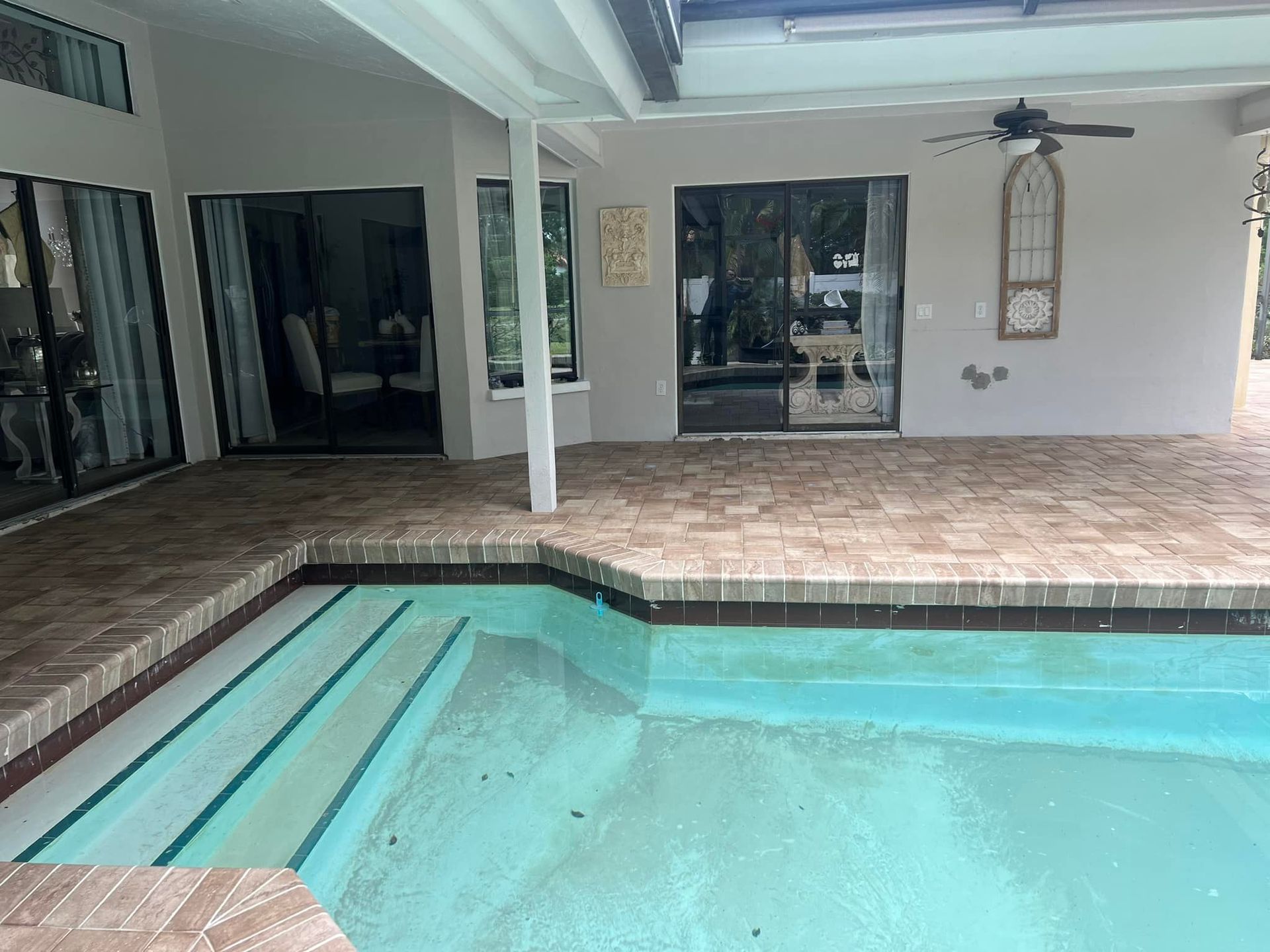 Poolside patio with steps into the pool, brick pavers, and sliding glass doors.