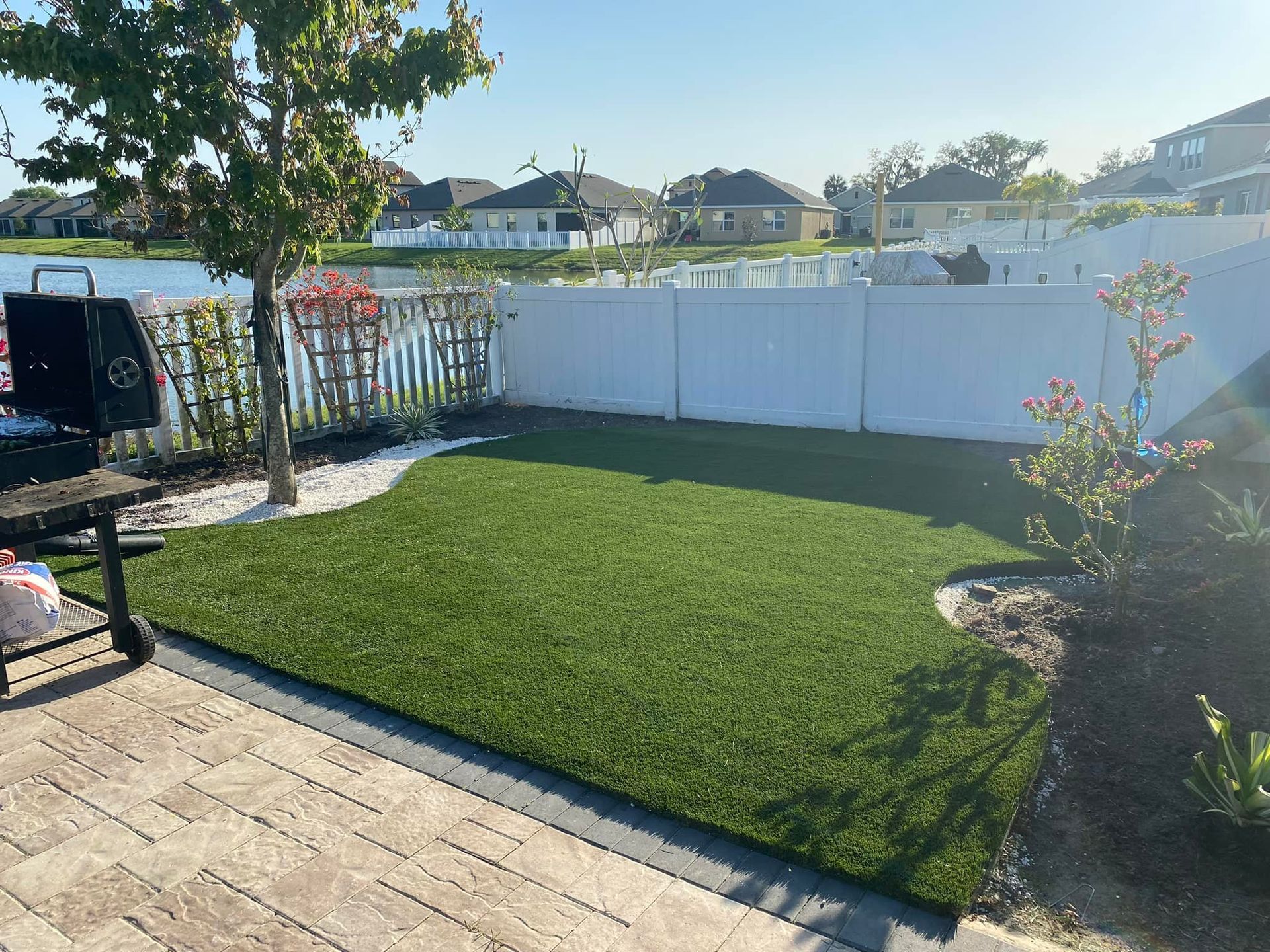 Backyard with green turf, white fence, lake view, and a grill.