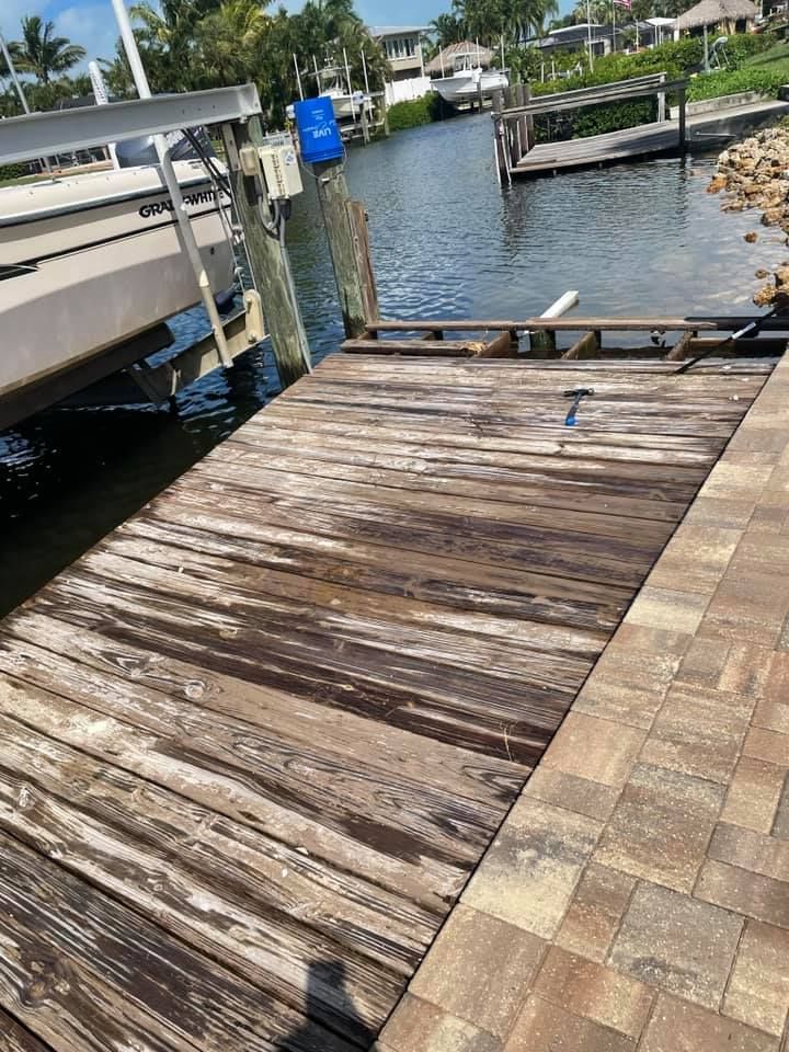 Wooden dock extending into water, next to a boat lift and a paved walkway.