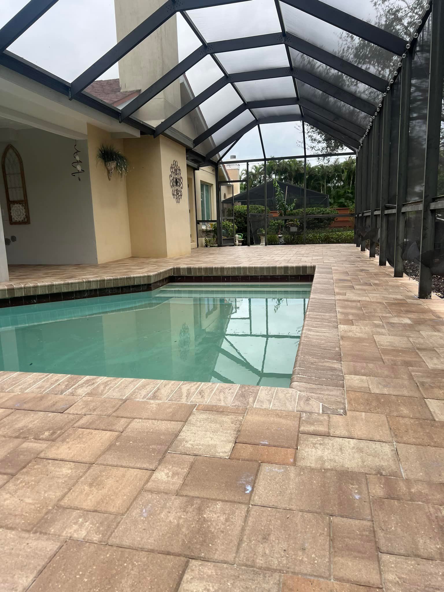 Pool area with screened enclosure, brick pavers, turquoise water. Sunny, outdoor setting.