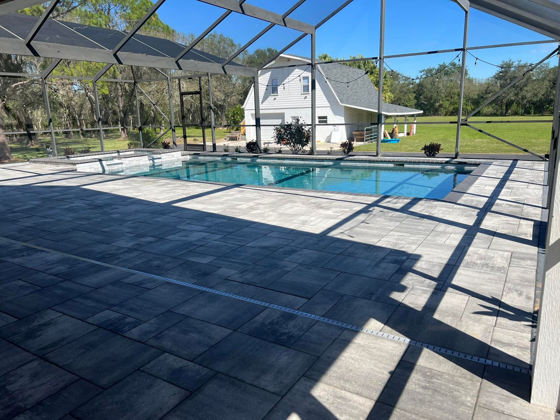 Screened-in pool and patio area, overlooking a grassy yard and white house on a sunny day.