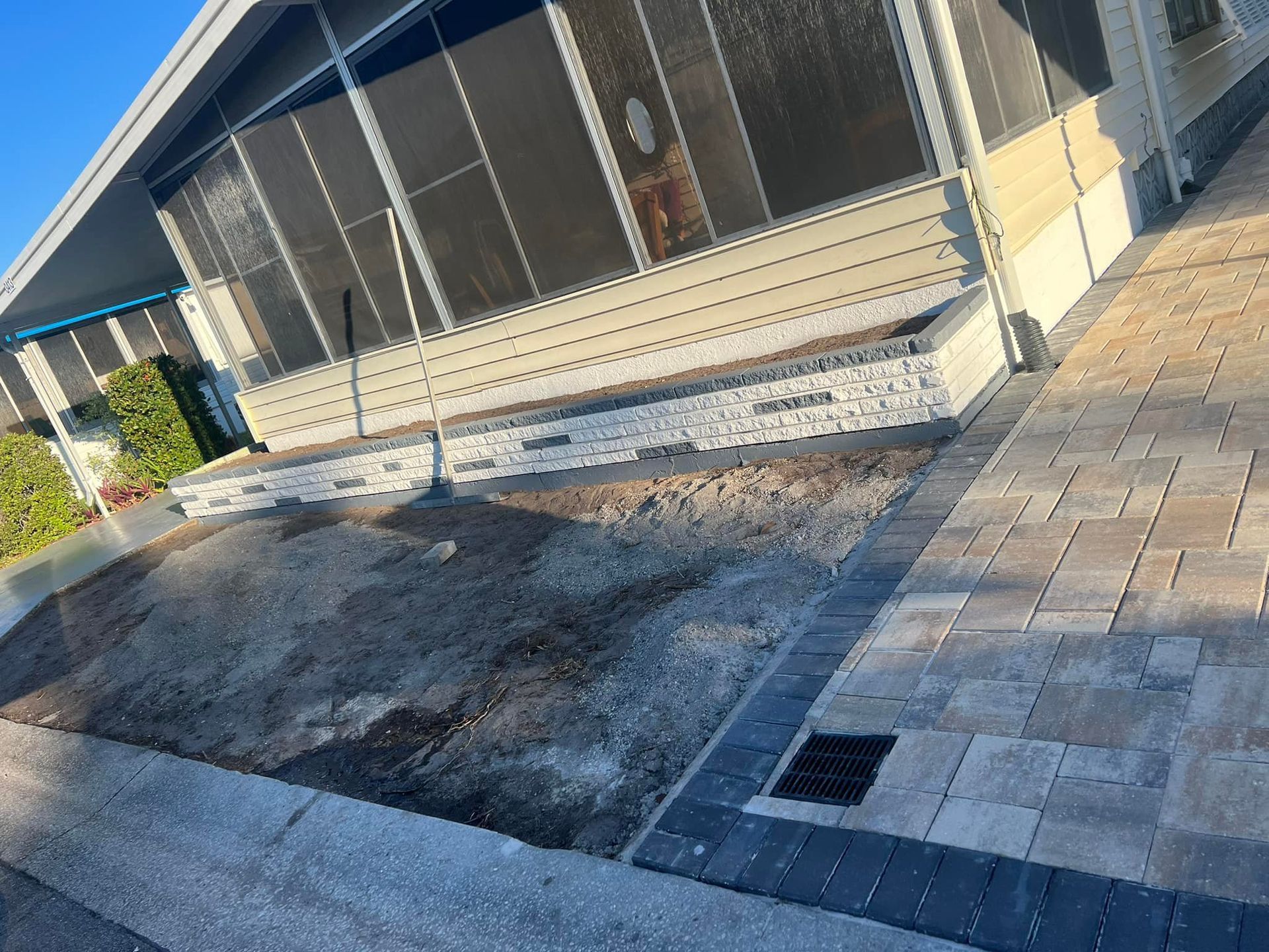 Exterior of a house with a concrete walkway, flowerbed, and screen porch. Ground is bare.