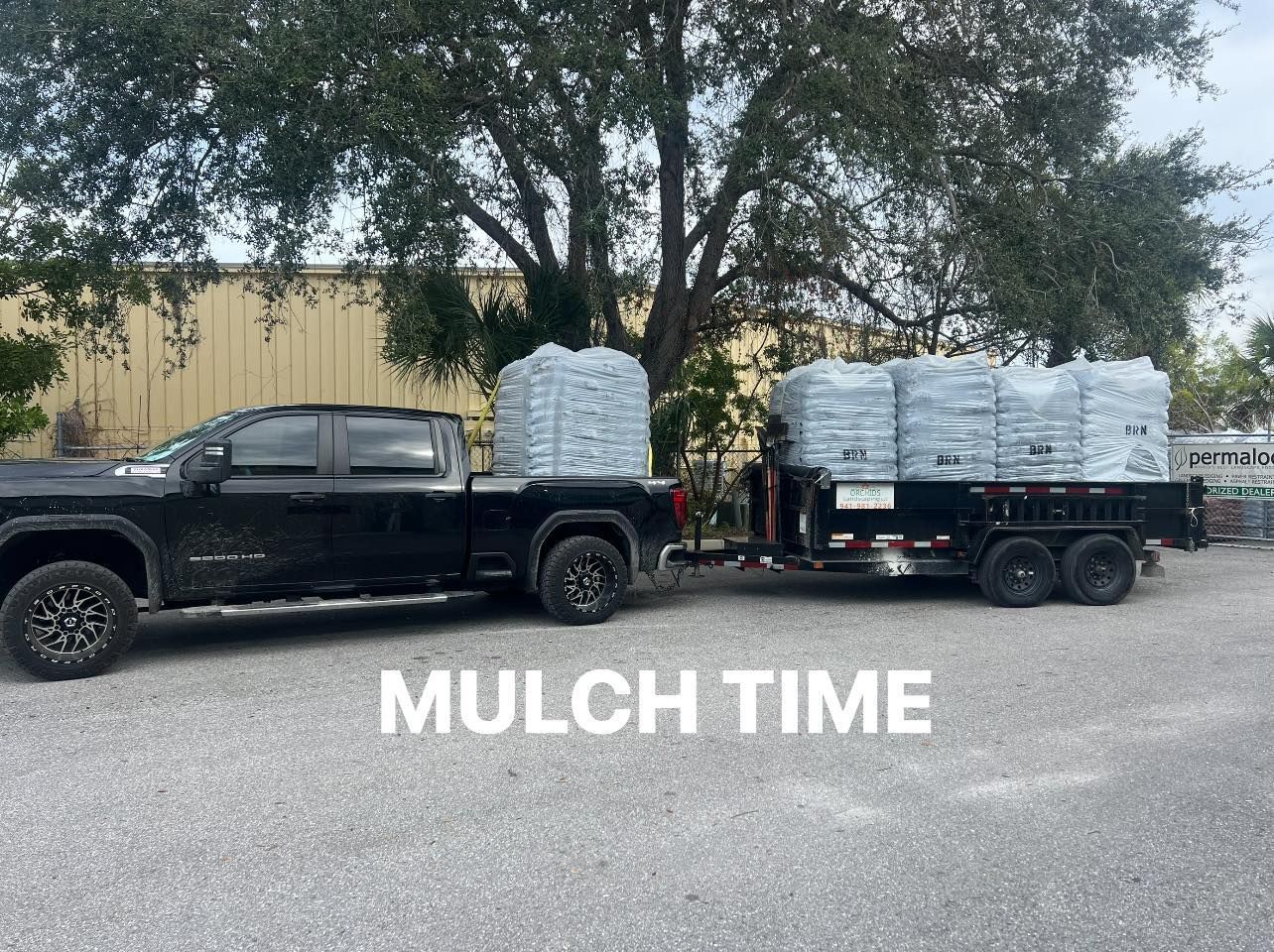Black truck towing a trailer loaded with bags of mulch on a paved surface, labeled 