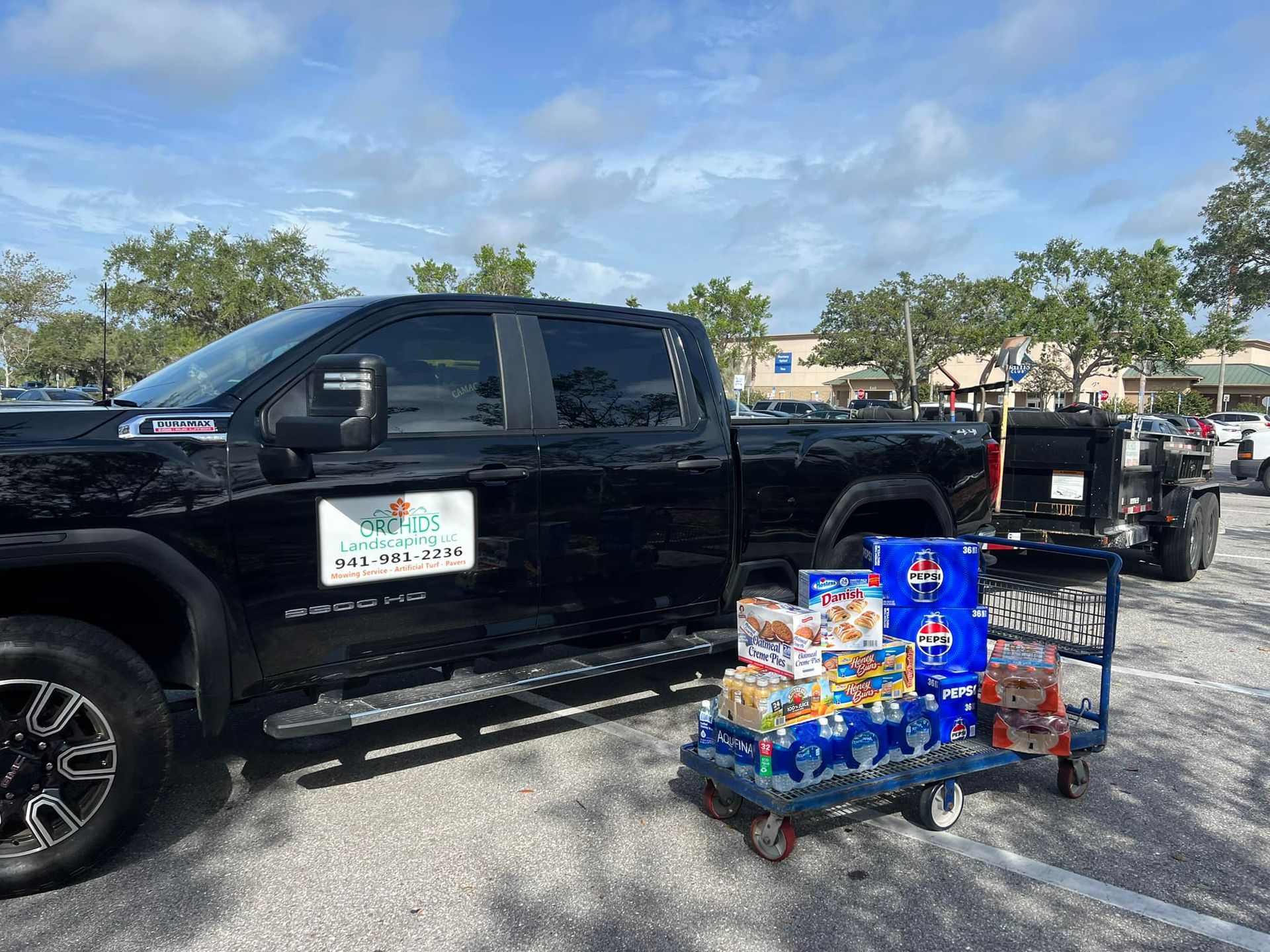 Black pickup truck with cart of supplies in a parking lot. Cloudy blue sky.