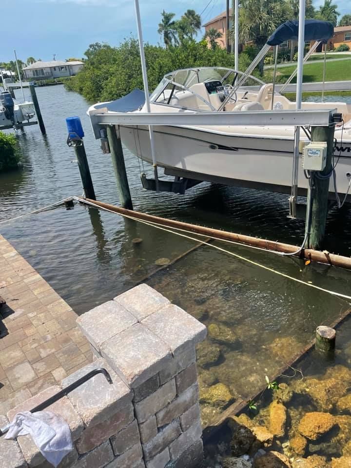 Boat docked at a pier with a lift, blue sky, water, and brick structure.