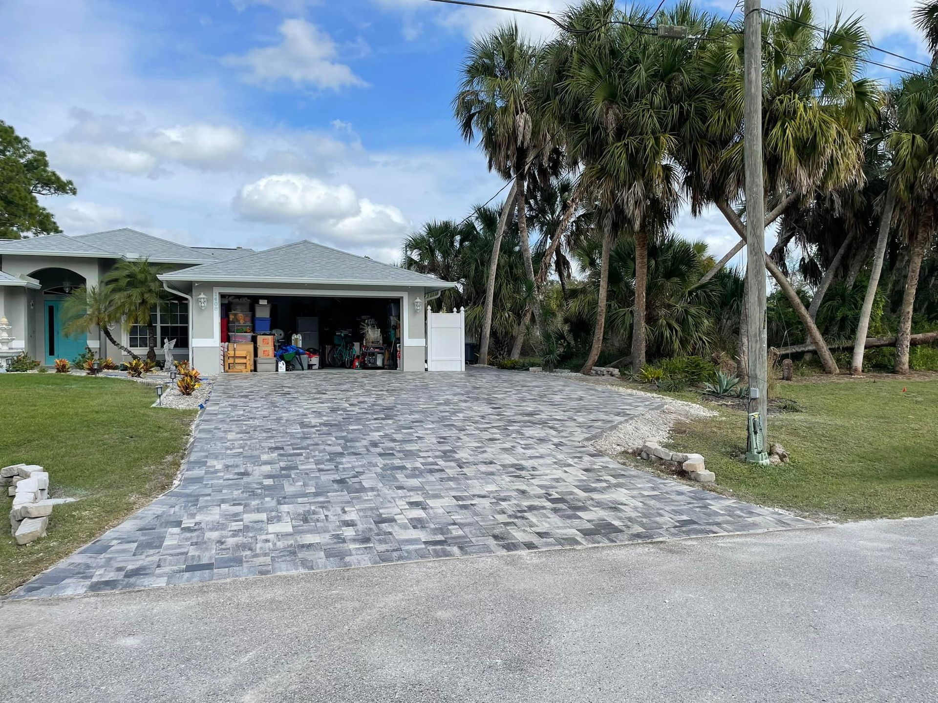 House with brick driveway, open garage, and palm trees in Florida.