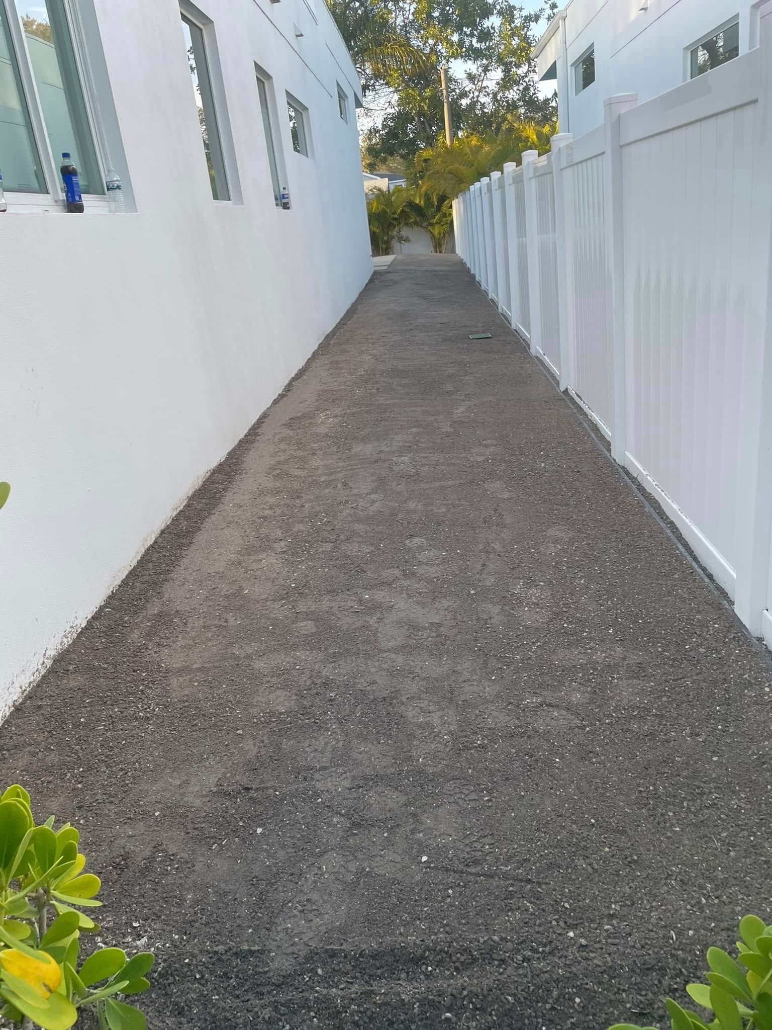 Gravel pathway between two white buildings and a white fence.