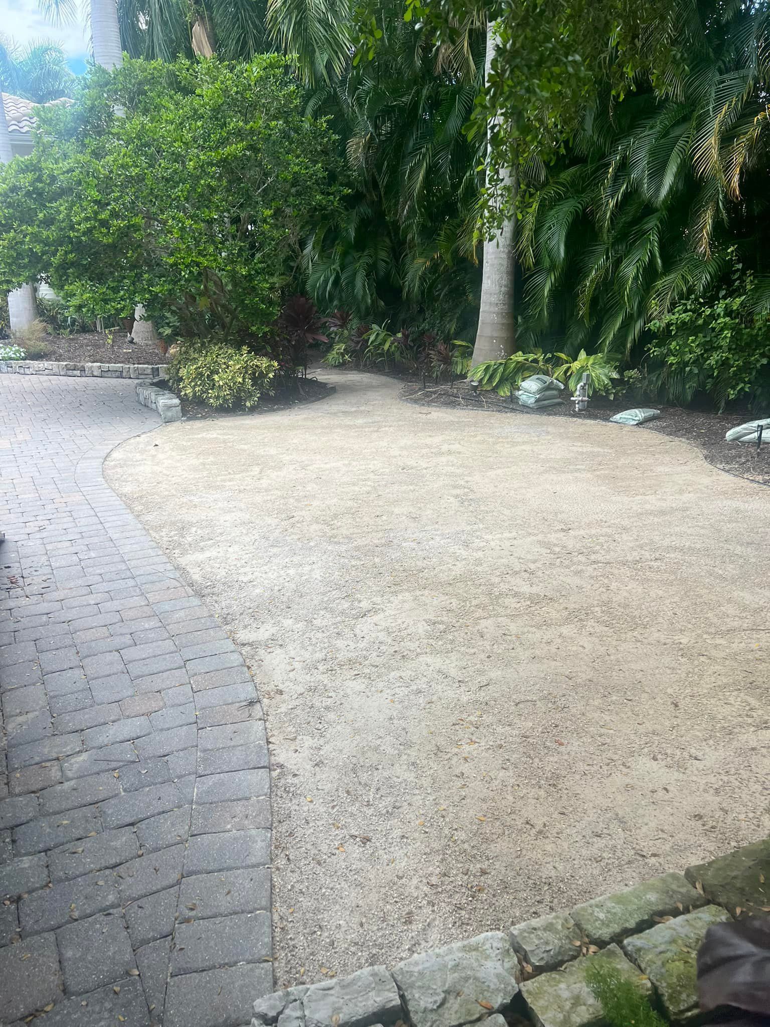 A gravel ground area surrounded by plants and brick path.