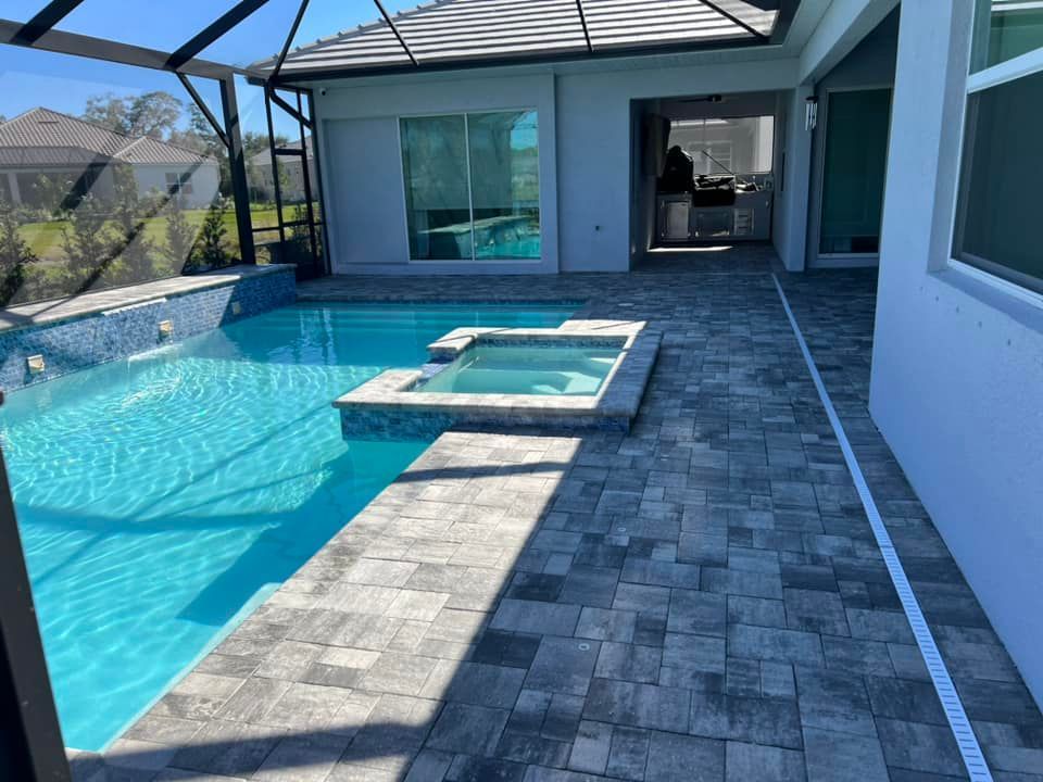 Pool and spa with gray pavers. Pool water is turquoise. Covered patio area.
