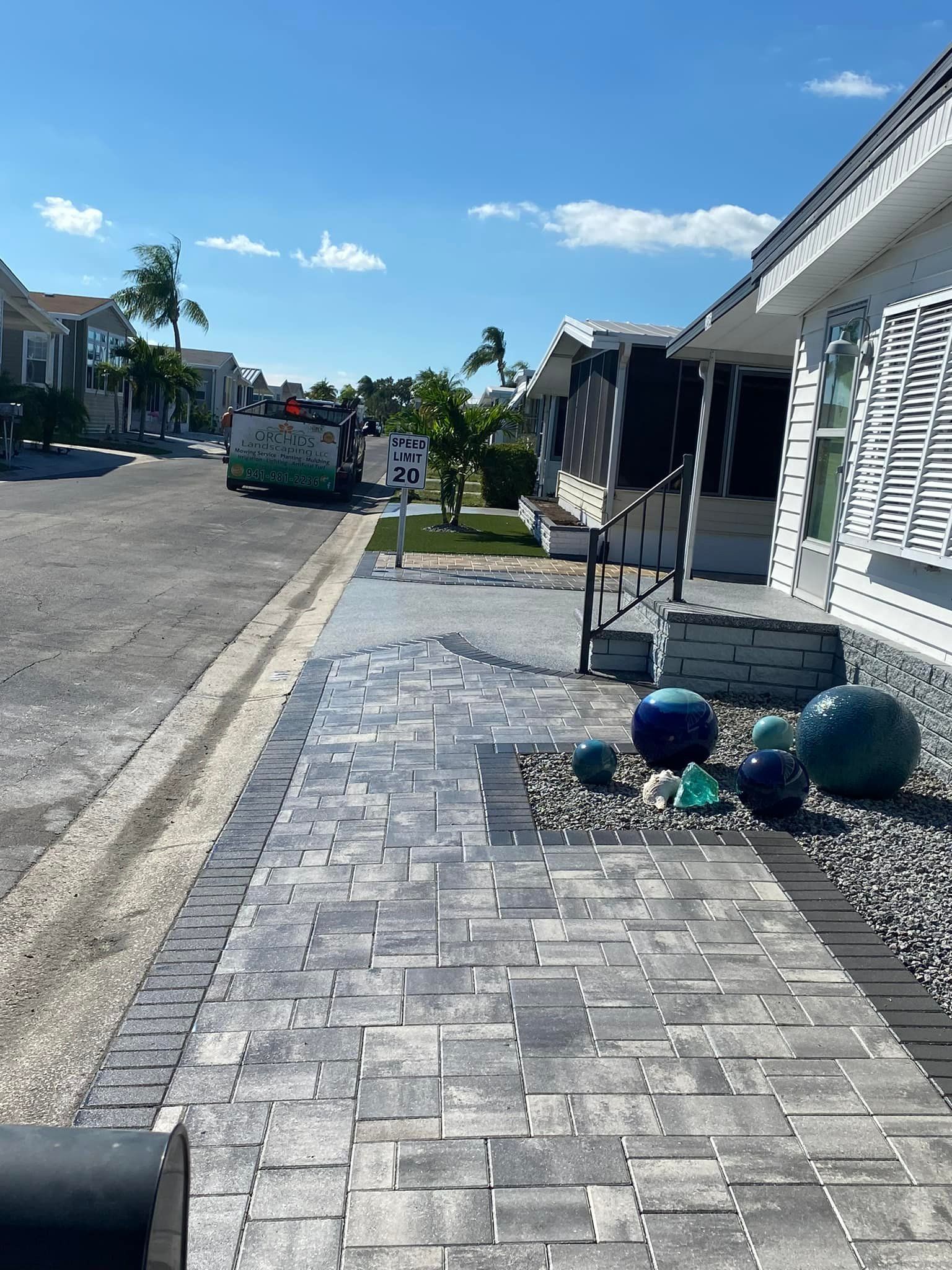 Brick walkway leading to a house with blue glass spheres on a gravel bed. A truck is parked on the street.