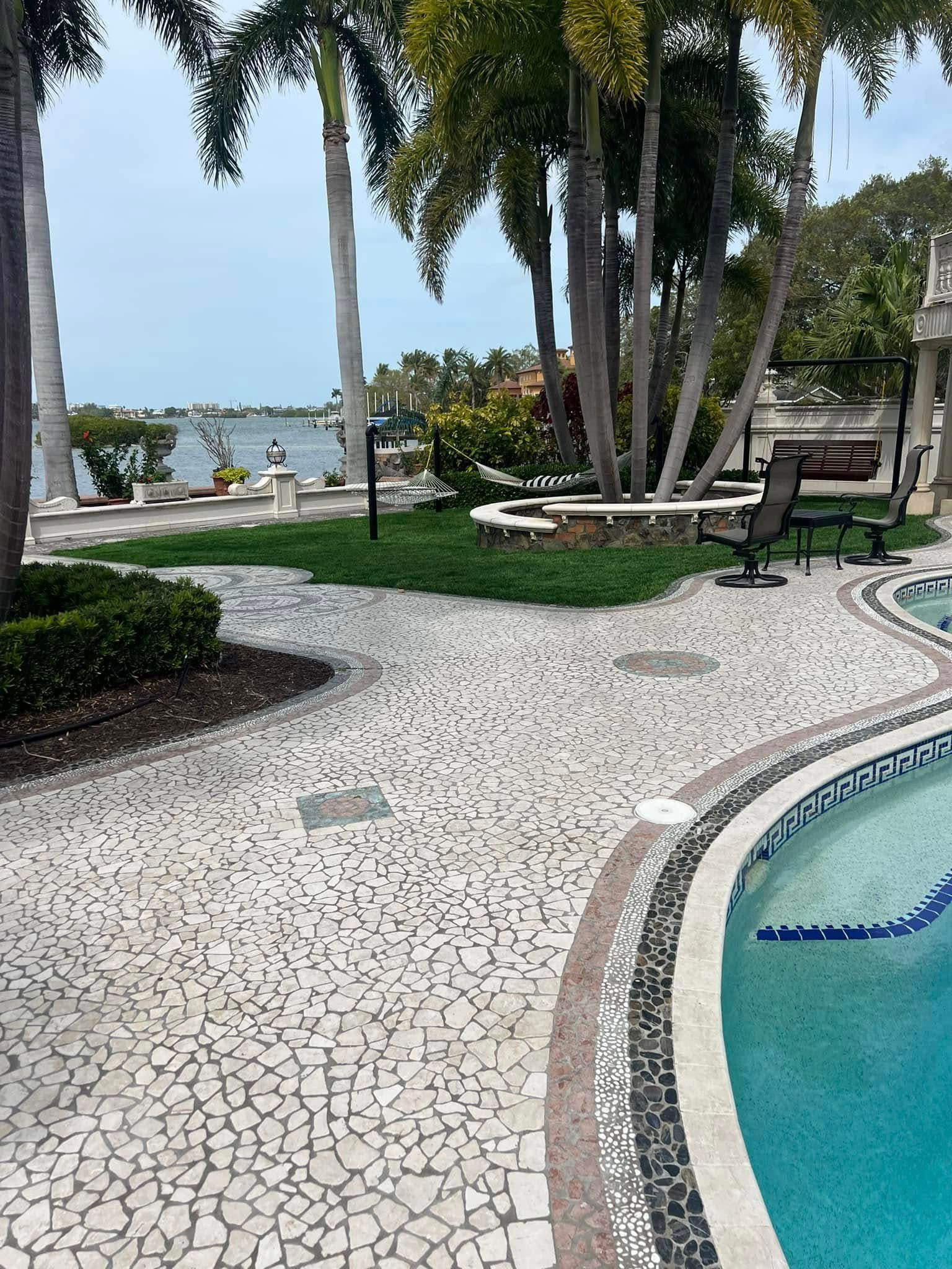 Poolside patio with mosaic tile walkway, palm trees, and water view.