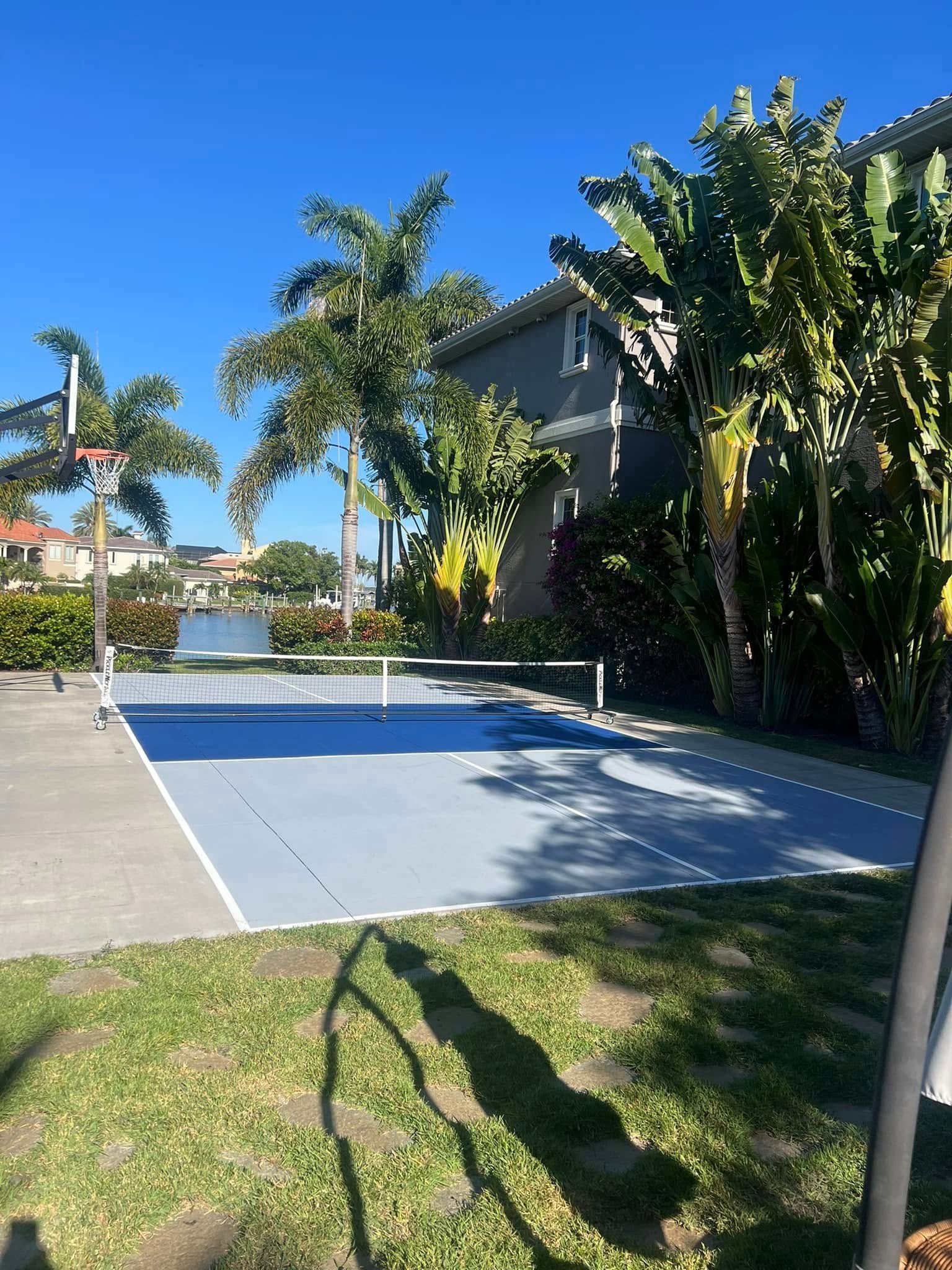 Outdoor basketball and pickleball court with lush tropical foliage and blue sky.