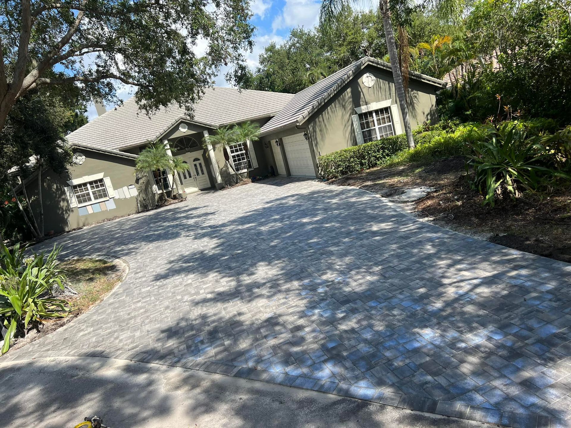 A light green house with a gray tile roof and a brick driveway on a sunny day.