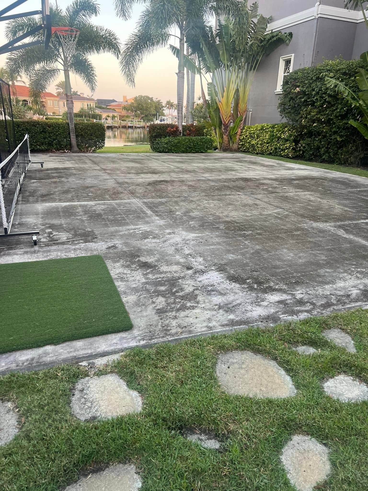 Outdoor concrete surface with a grass area and stepping stones. Trees and a lake in the background.