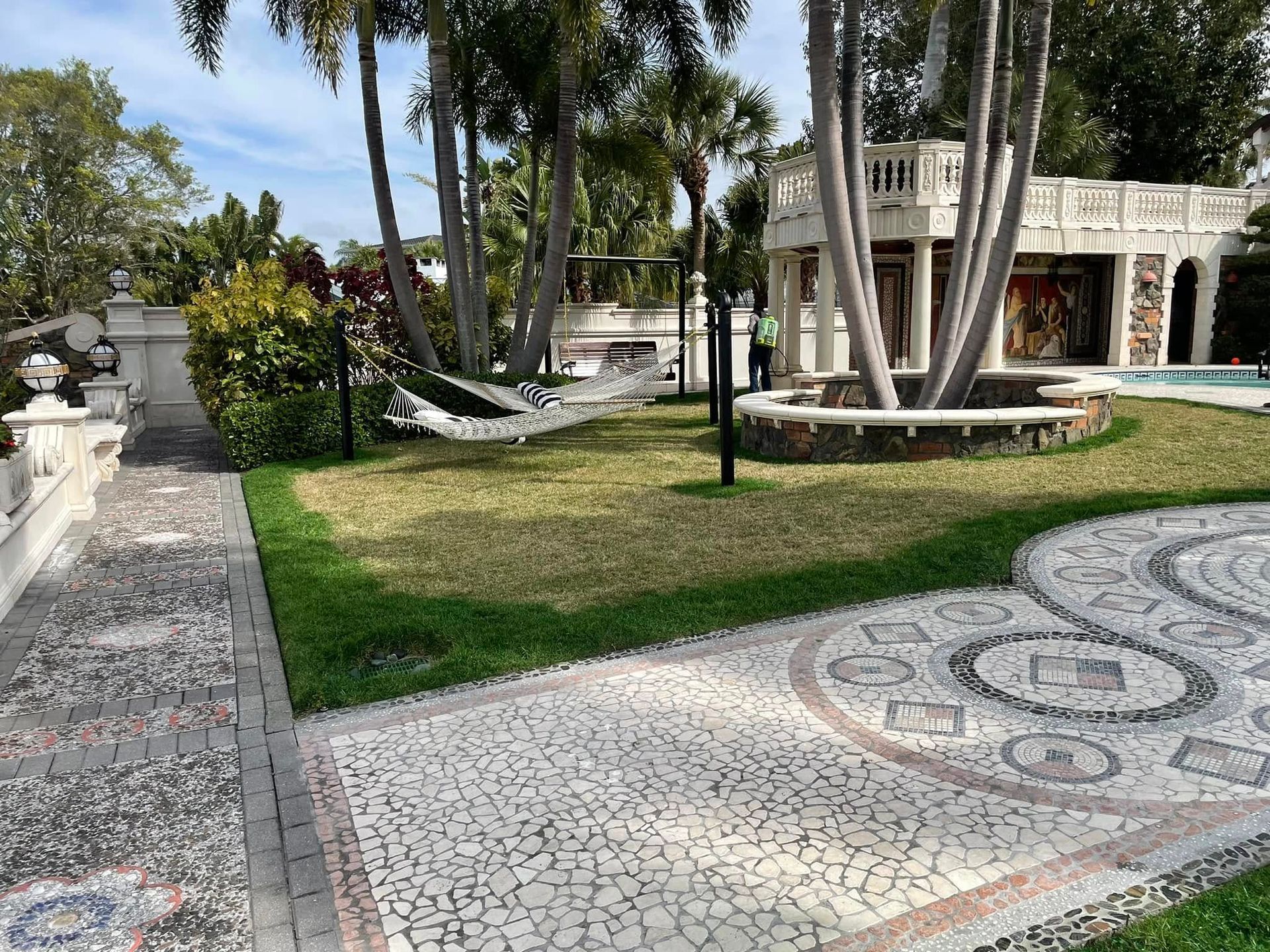 Lush backyard with mosaic pathway, hammock, and ornate stone structure.