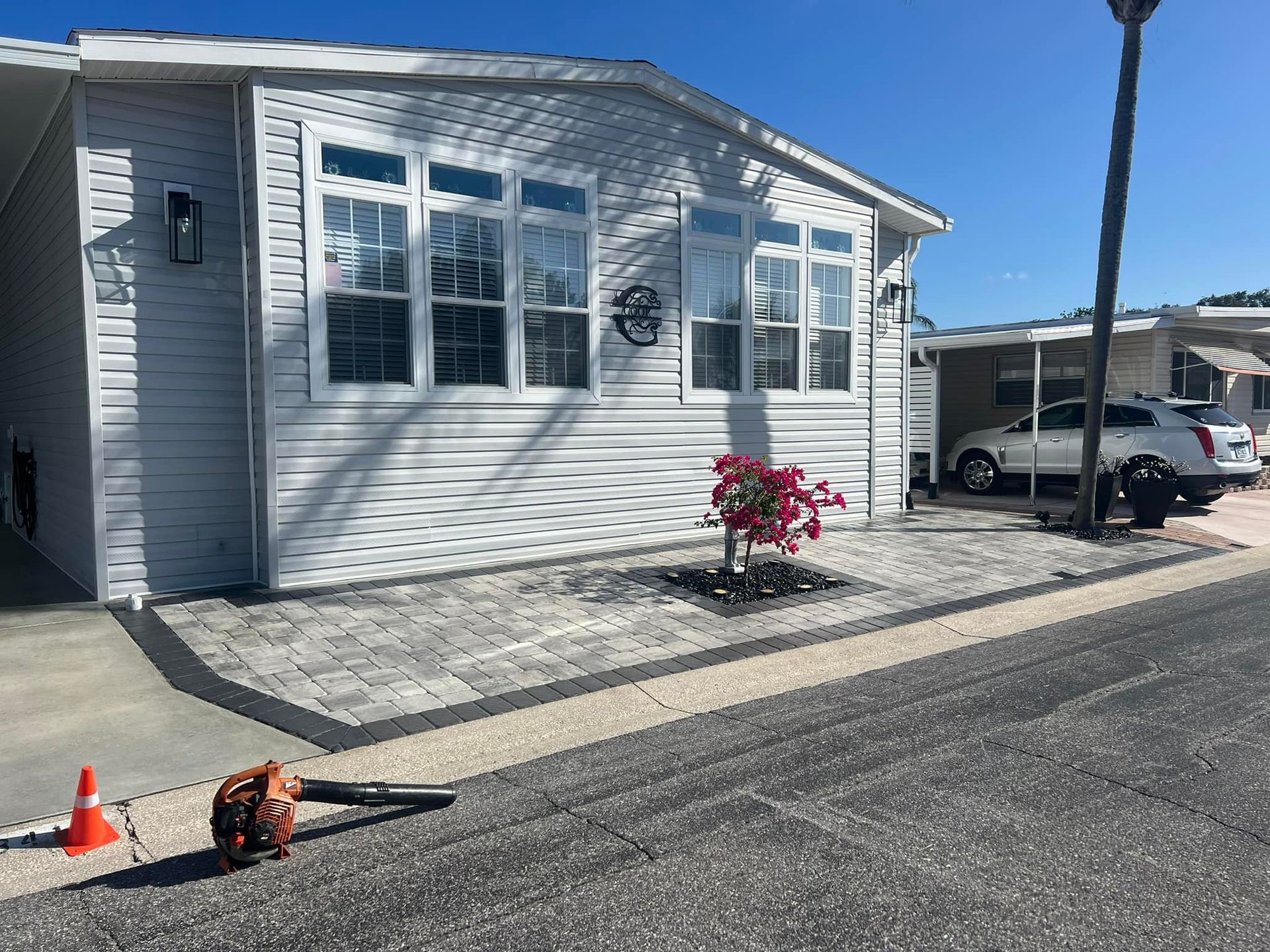 Mobile home with gray siding, white trim, and a small flowerbed. Paved walkway in front.