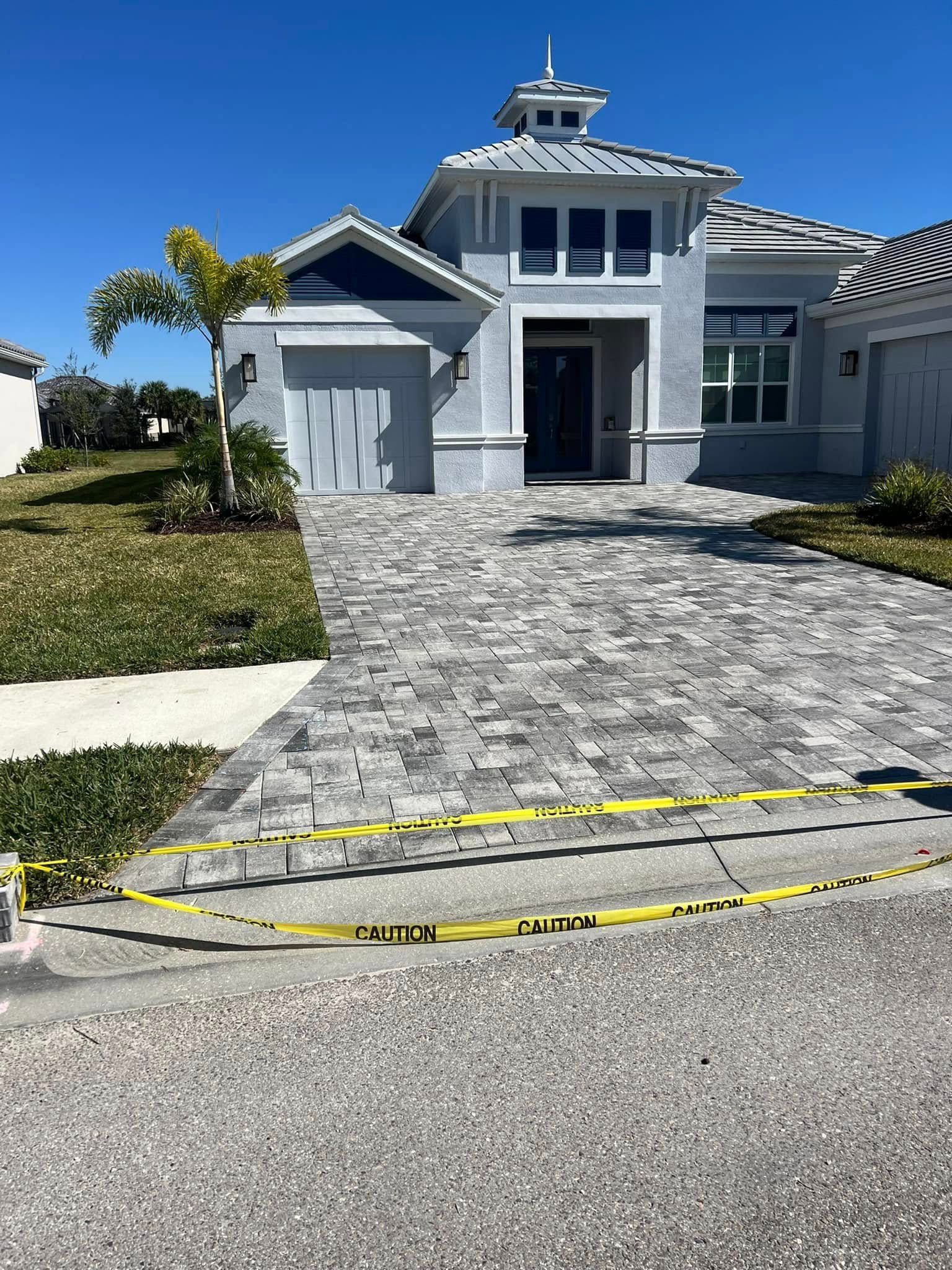 A light gray house with a stone paver driveway, yellow caution tape on the ground.