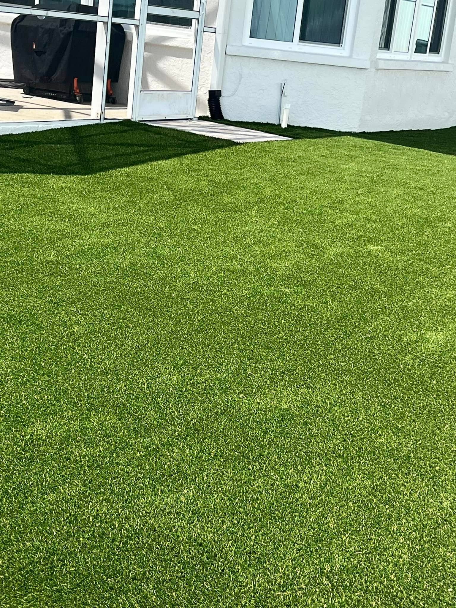 Artificial green lawn in front of a white building with windows.