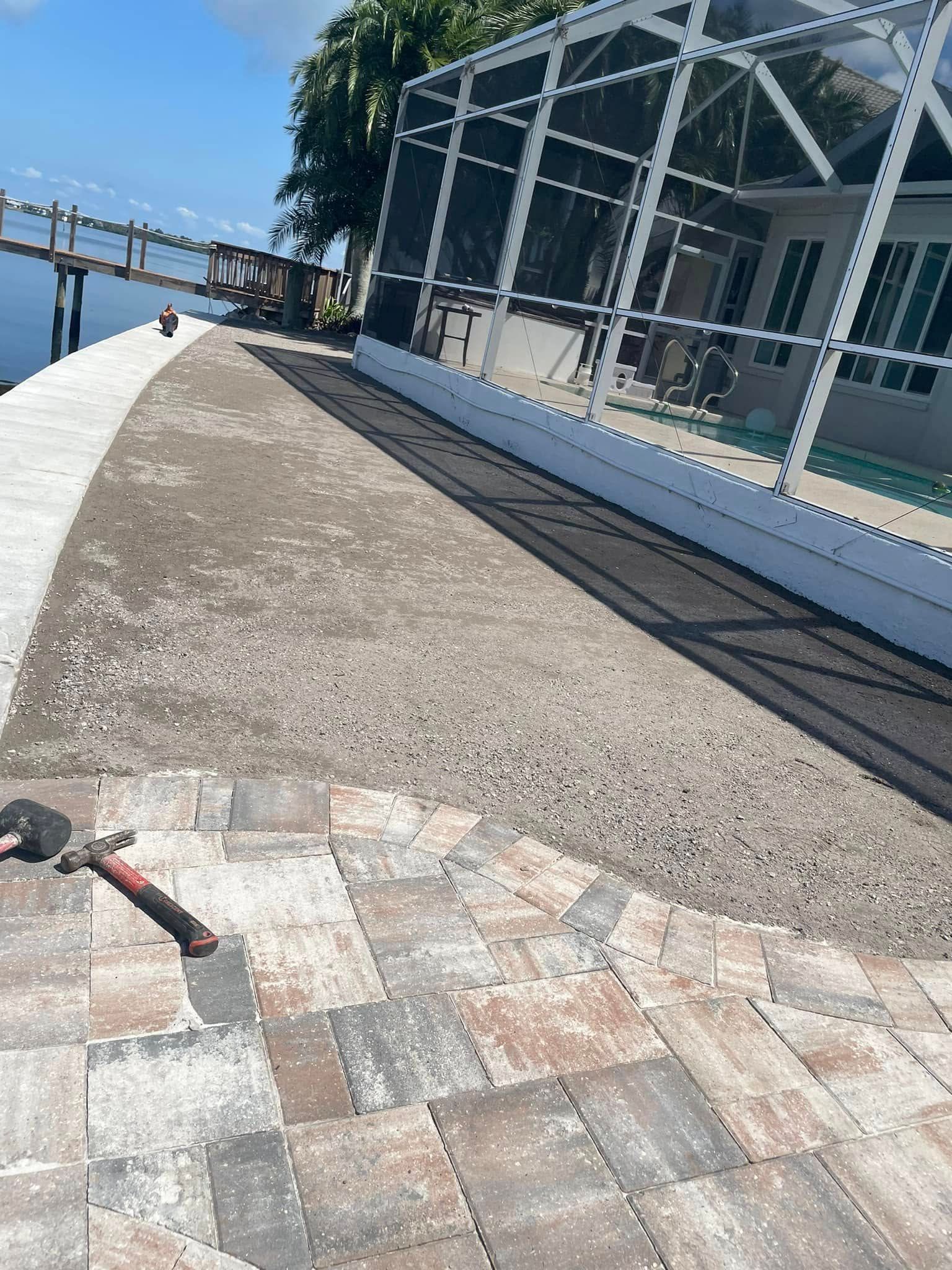 Paved area under construction with a pool screen enclosure and a waterfront dock in the background.