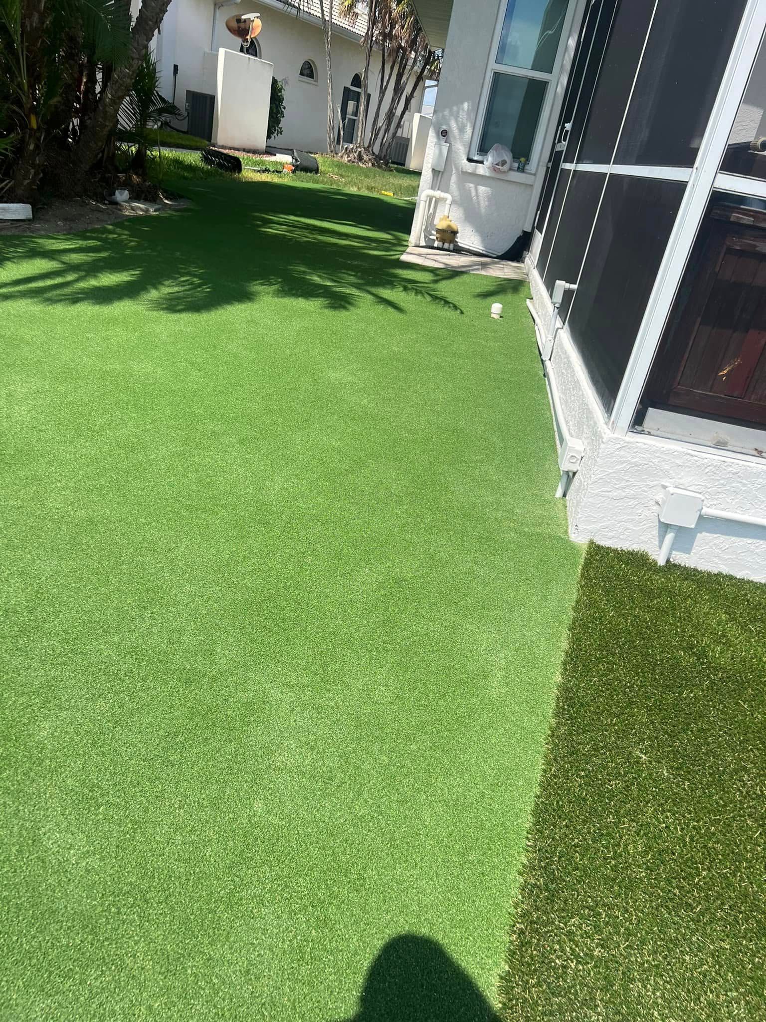 Green artificial turf lawn next to a white house with a screened porch on a sunny day.