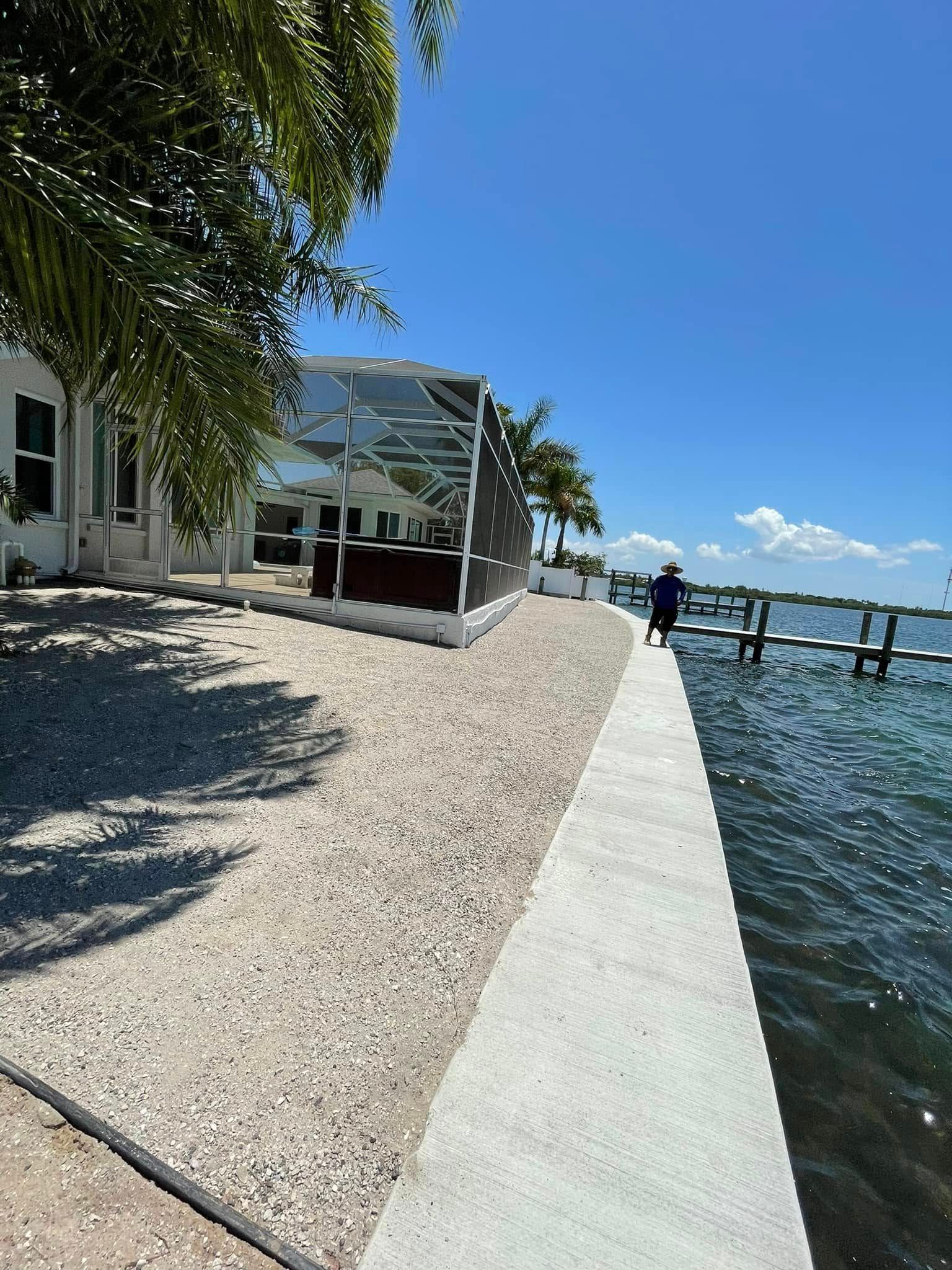 Waterfront home with a screened enclosure and a person walking on a concrete pathway. Blue sky.