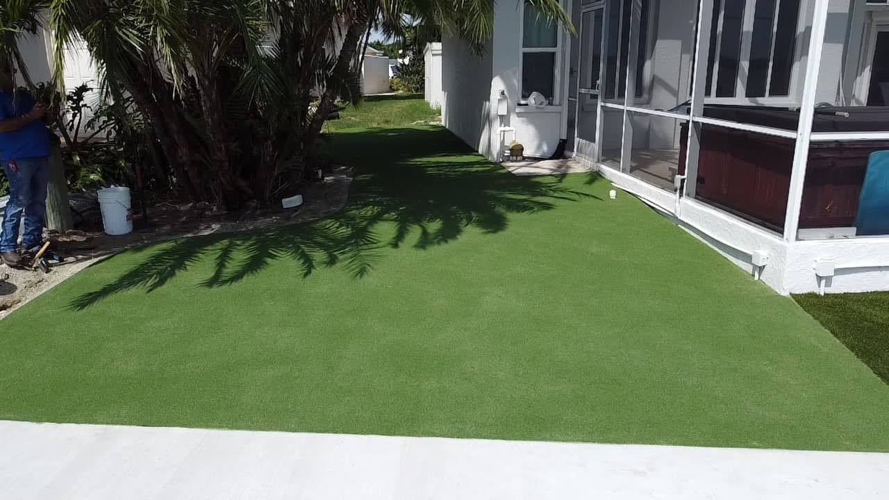 Green artificial turf installed next to a house with a white exterior. A person is visible in the background.