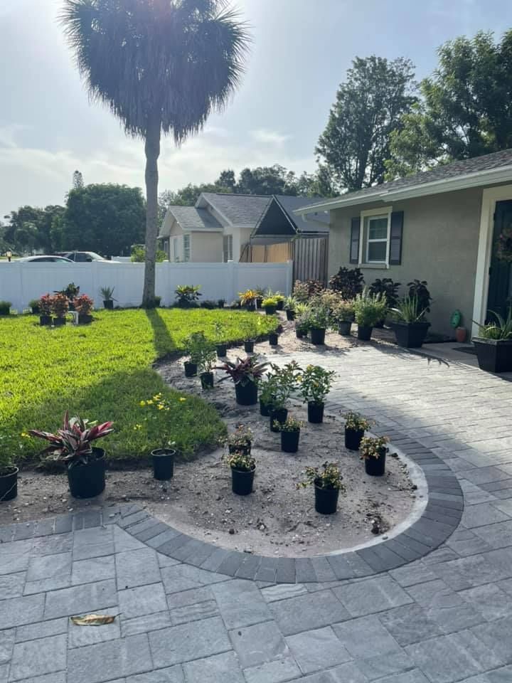 A yard with new paving and a circular garden bed filled with potted plants and surrounded by grass.