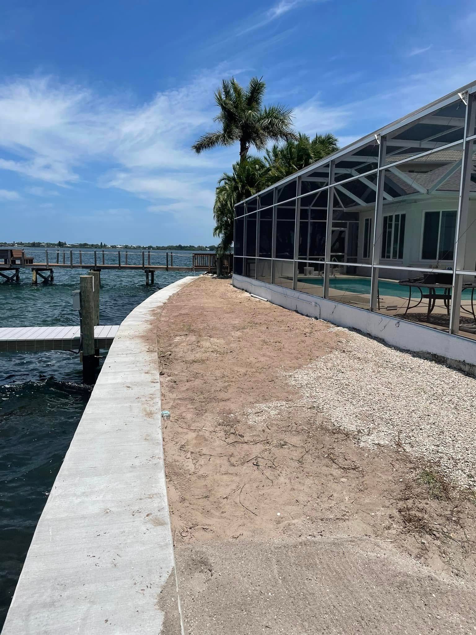 A waterfront property with a concrete walkway, dirt path, and screened porch on a sunny day.