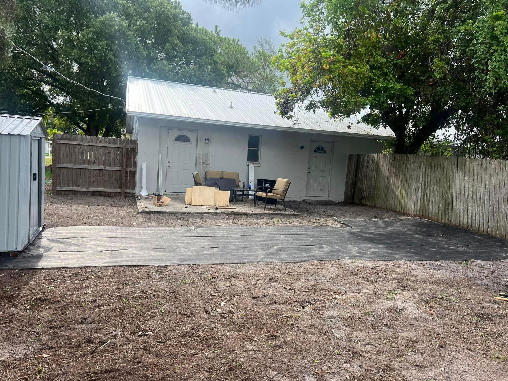 Backyard with a small white building, shed, and gravel ground cover. A patio area is visible.