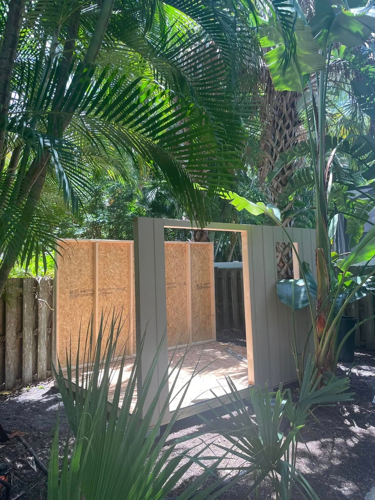 Partially constructed shed in a lush, green yard; OSB walls, doorway, and foliage visible.