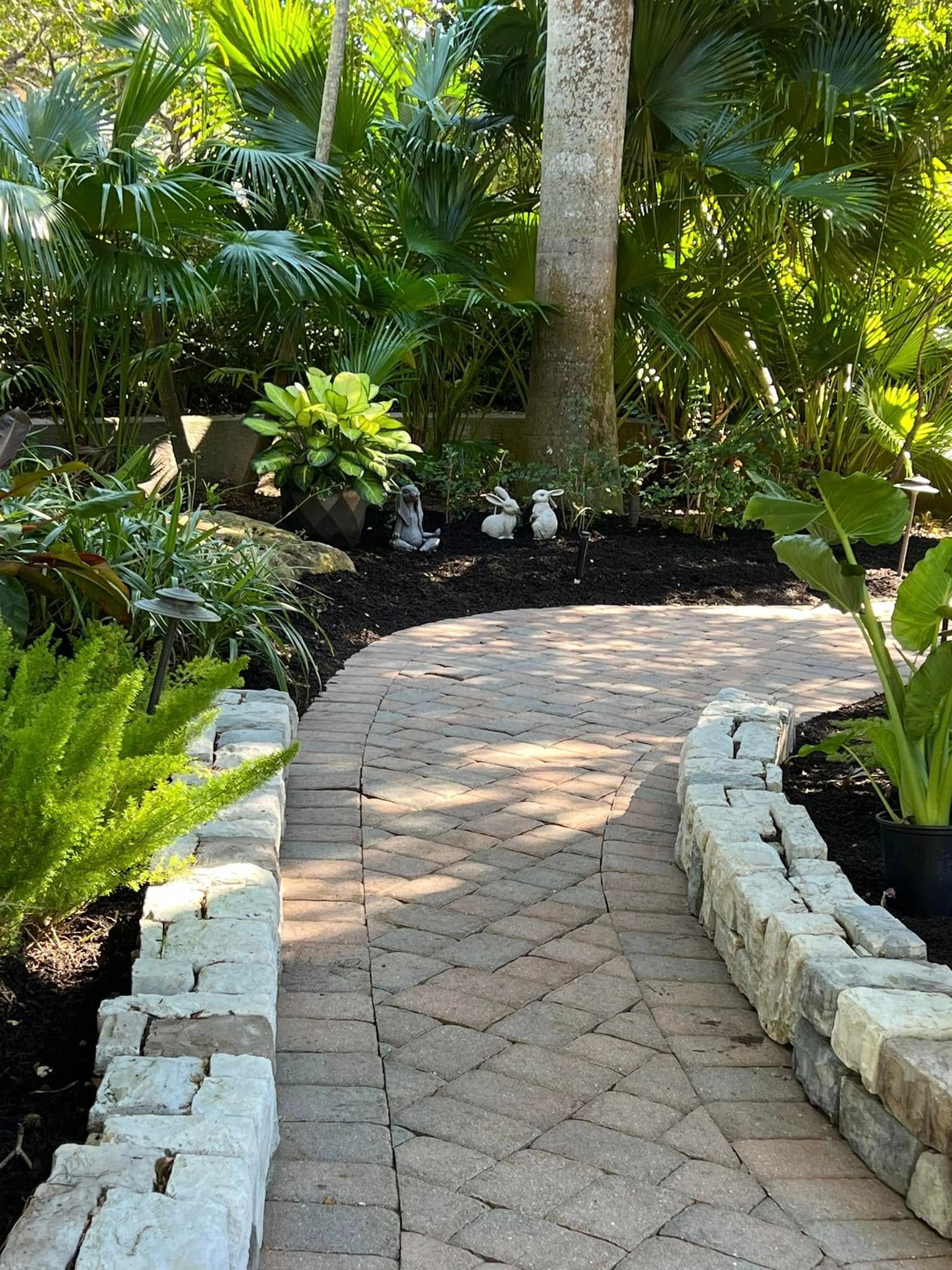 Brick path through a lush garden with dark mulch and stone borders.