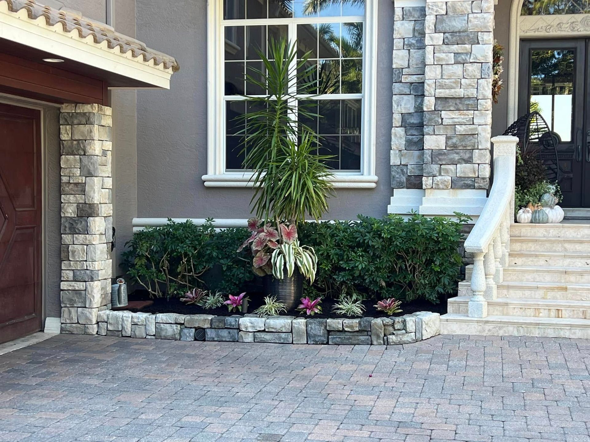 Exterior of a house with stone accents, a landscaped flower bed, and a brick driveway.
