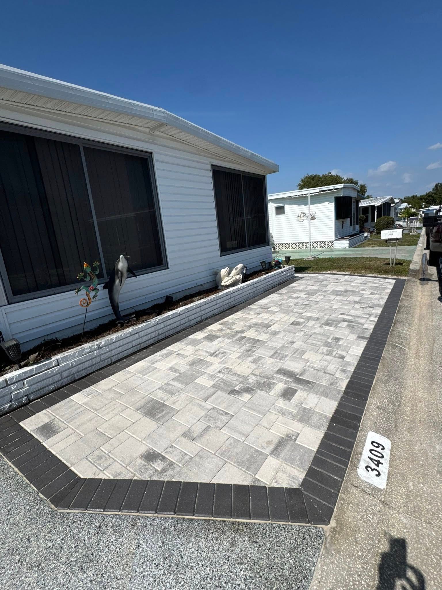 Paver patio beside a white house with black trim and a dark border. Street address is visible.