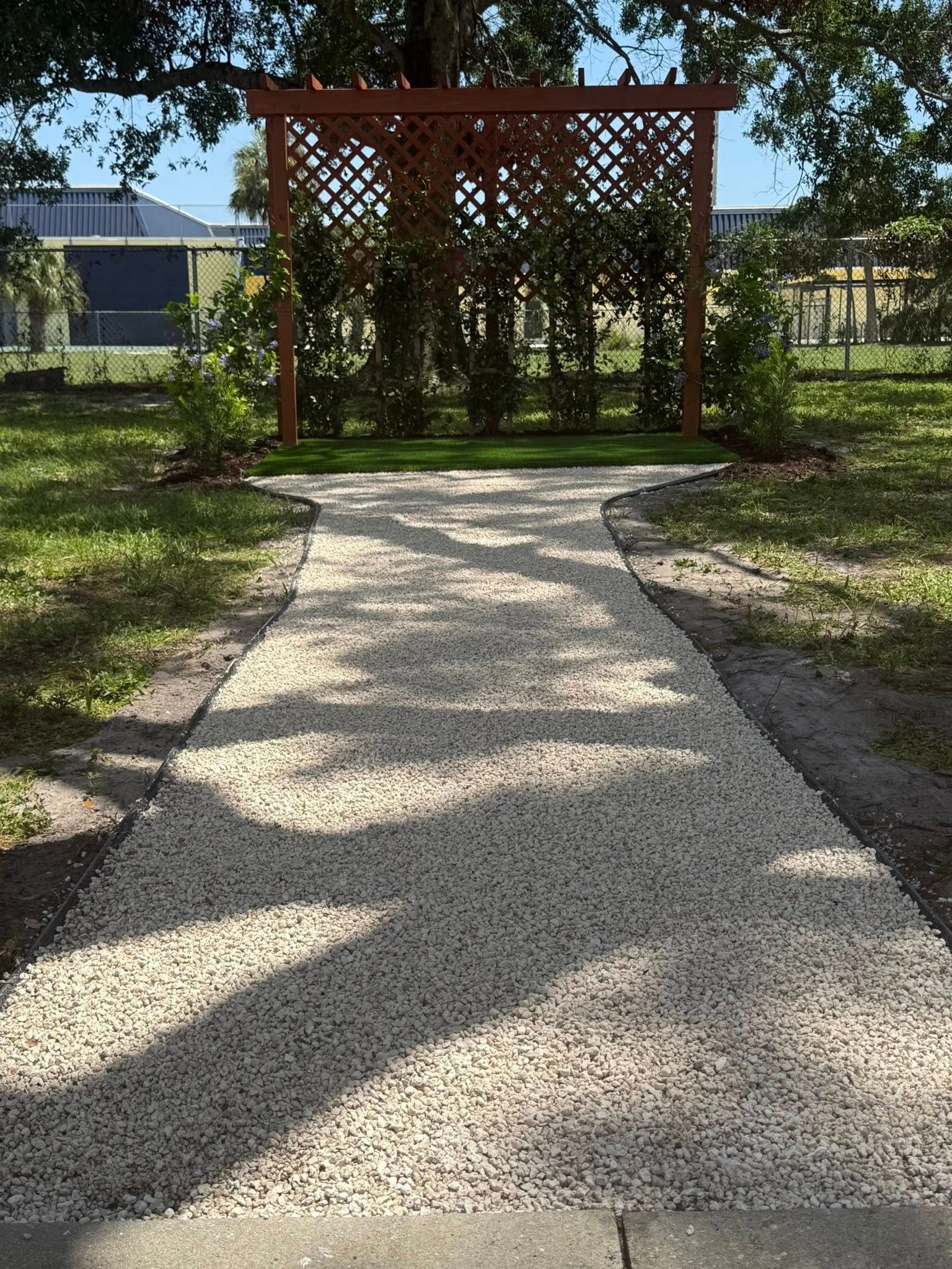 Gravel path leads to a wooden arbor in a garden.