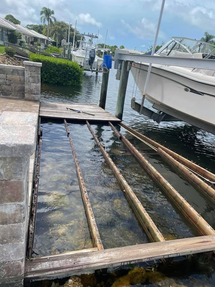 Wooden boat ramp submerged in water next to a pier. Boats and waterfront houses in the background.