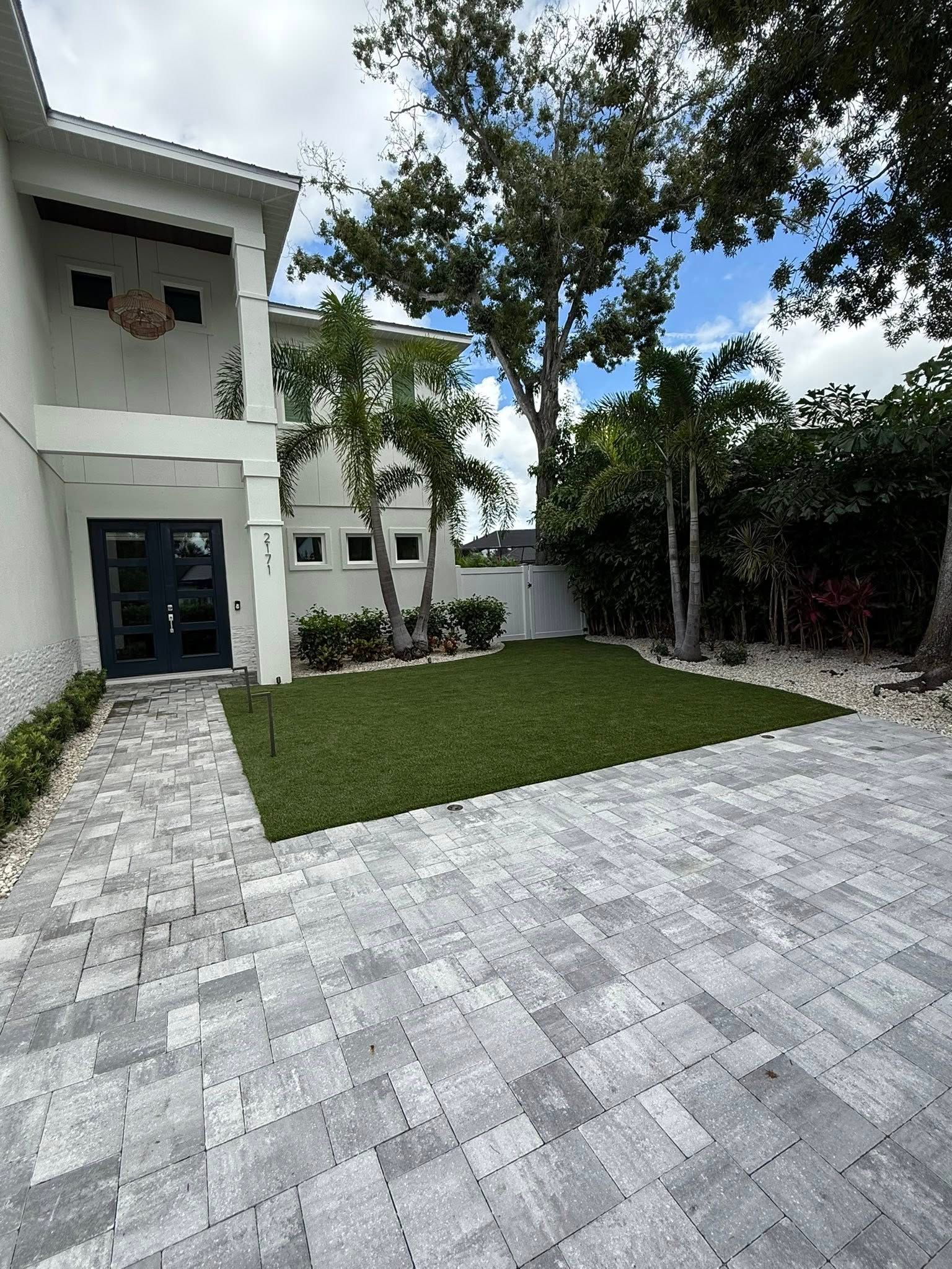Exterior view of a modern white house with a paved driveway, green lawn, and trees.