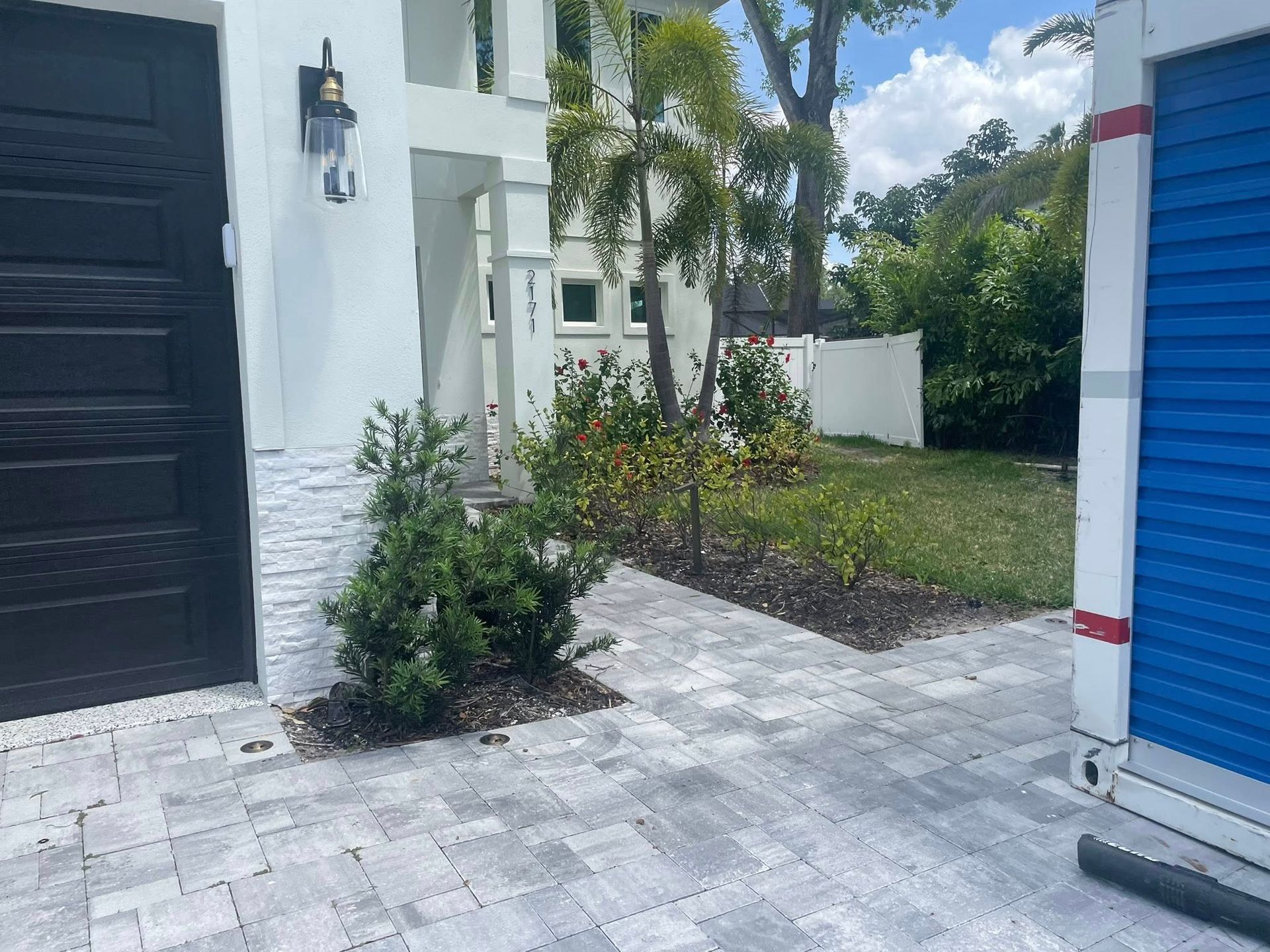 Exterior of modern house with paved path, landscaping, and a blue storage unit.