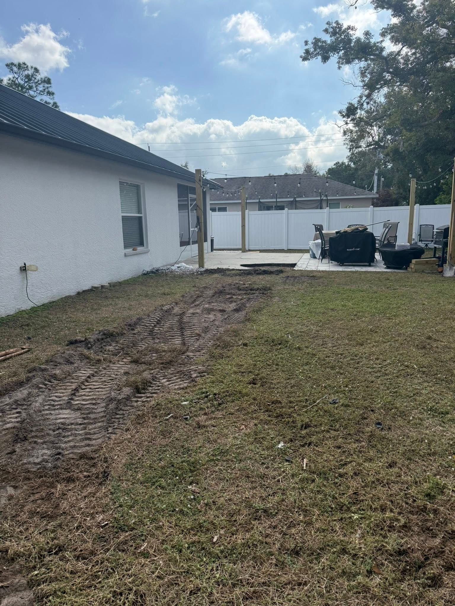 Backyard with dirt path, patio, house, and wooden posts under a cloudy sky.