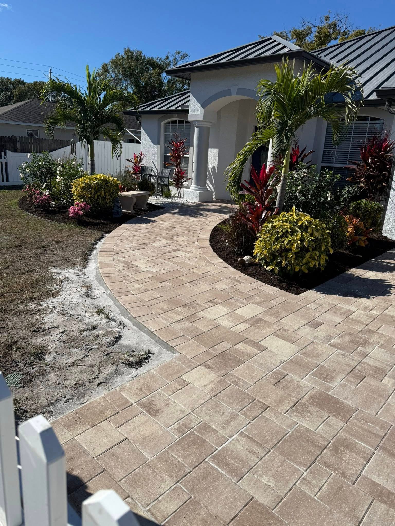 Brick walkway leading to a white house with landscaping. Sunny day.