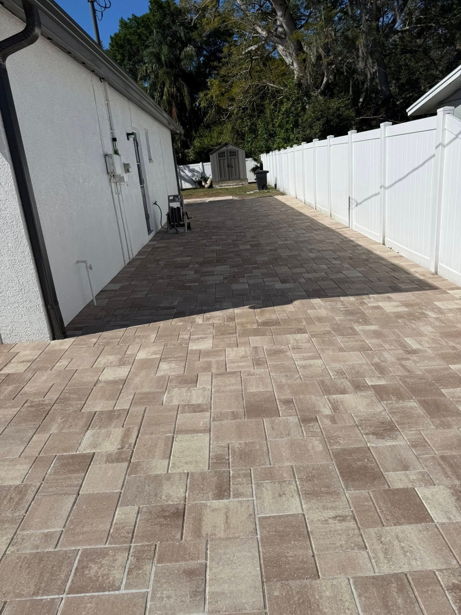 Brick paved patio with a white fence, adjacent building.