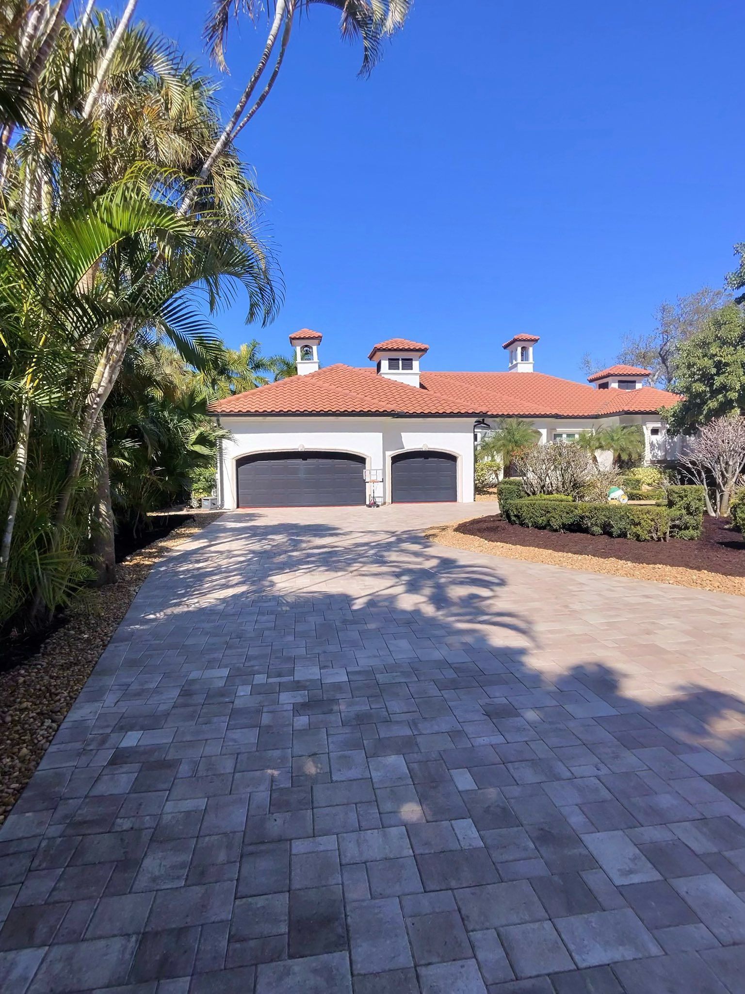 A white multistory home with a modern geometric paver driveway, landscaping, a parked car, and a golf cart.