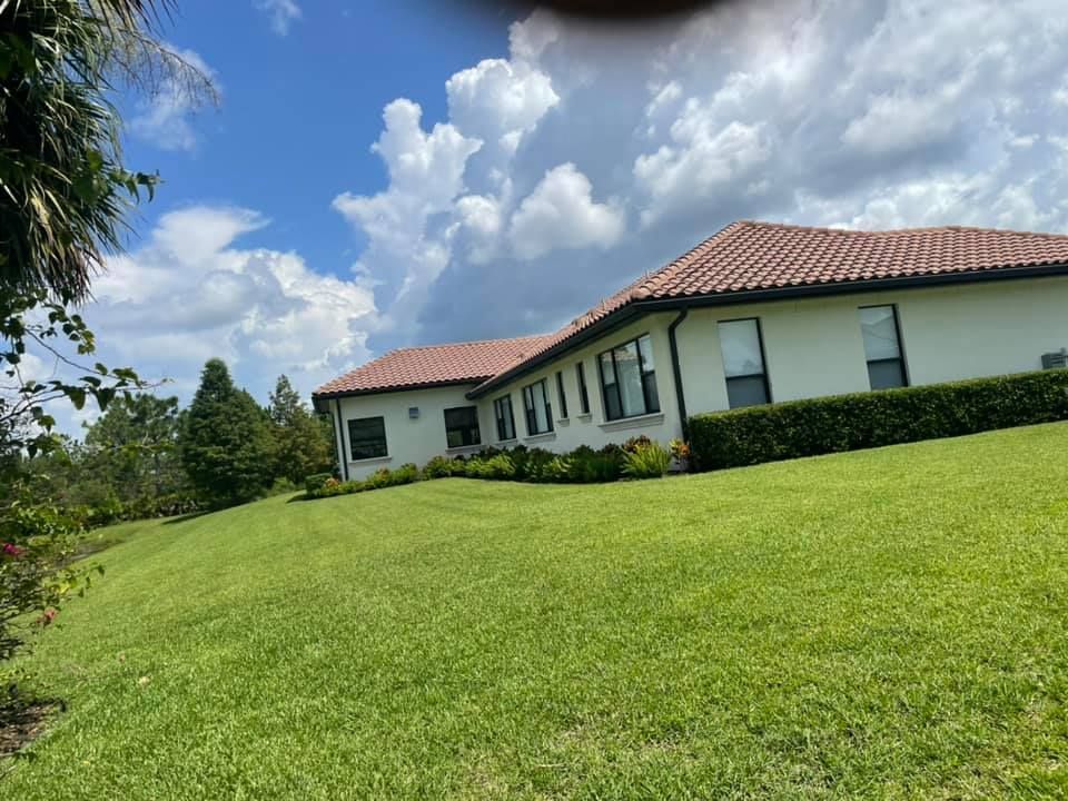 White house with red tile roof on a grassy hill under a cloudy blue sky.