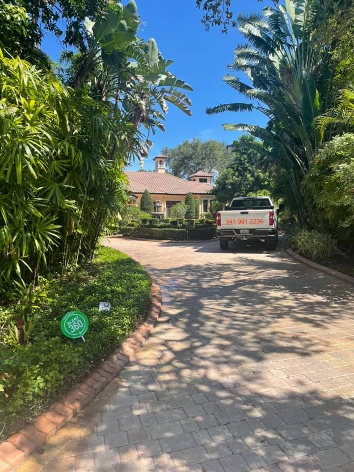Paved driveway leading to a house, a white truck parked in front. Lush greenery and blue sky.