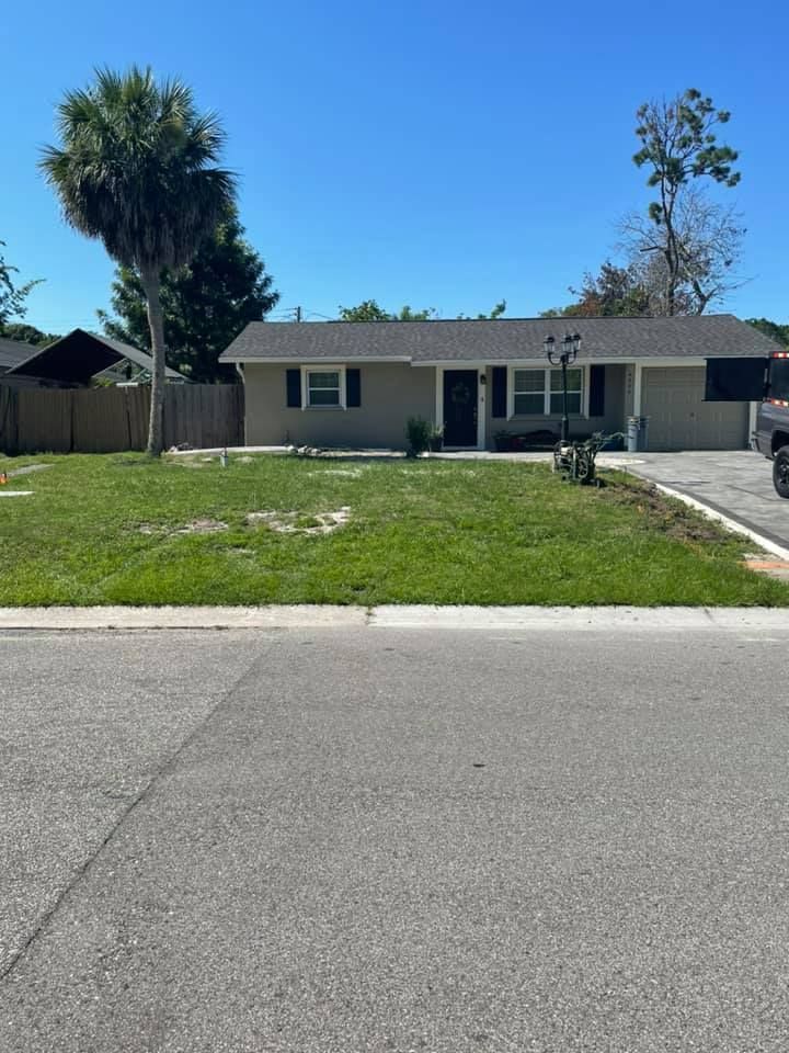 Single-story beige house with green lawn, driveway, and blue sky.